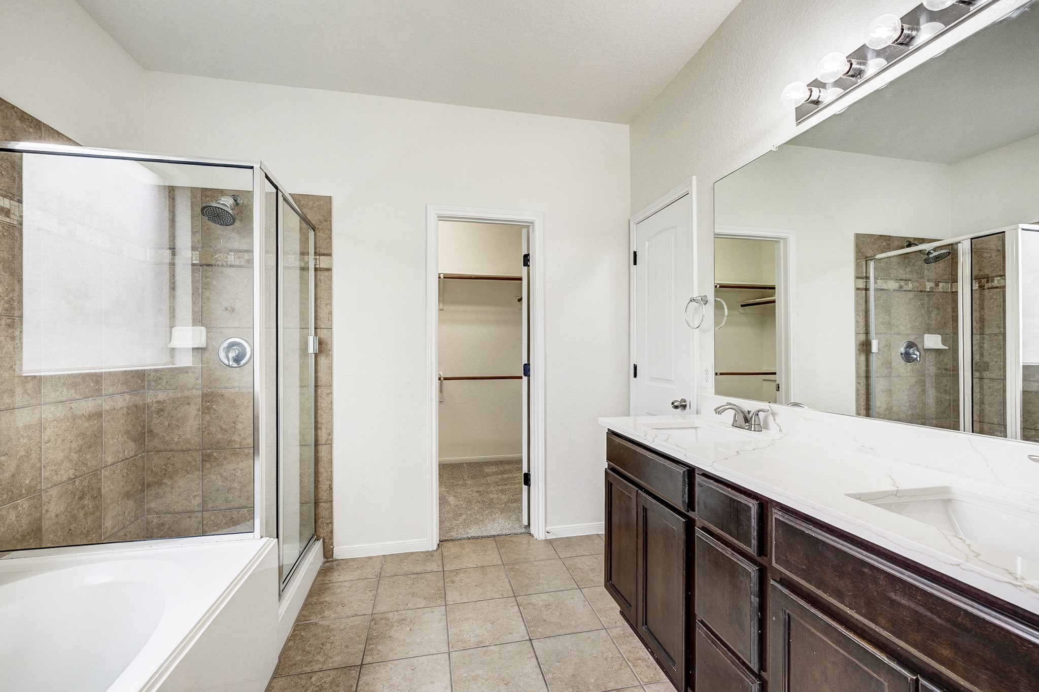 Spacious bathroom featuring a dual-sink vanity, glass-enclosed shower, and a relaxing bathtub, with direct access to a walk-in closet.