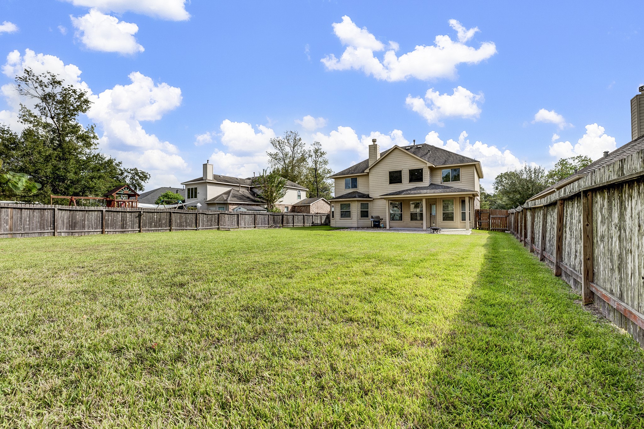Expansive backyard with lush green lawn and a spacious two-story home, perfect for family gatherings and outdoor activities.