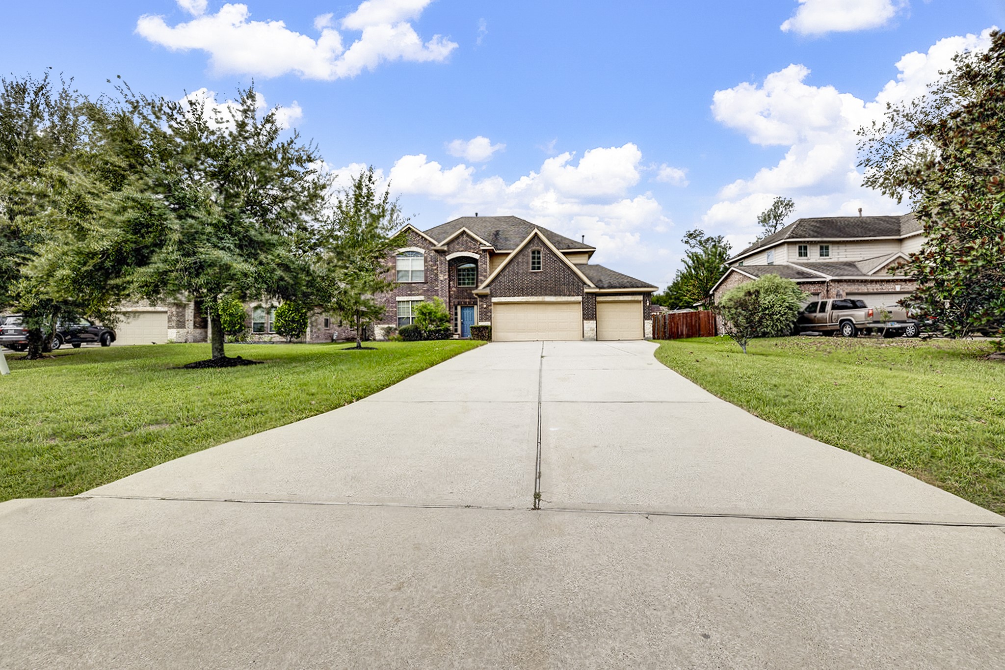 Stunning two-story brick home with a spacious three-car garage, set on a beautifully landscaped lot with a long driveway and mature trees.