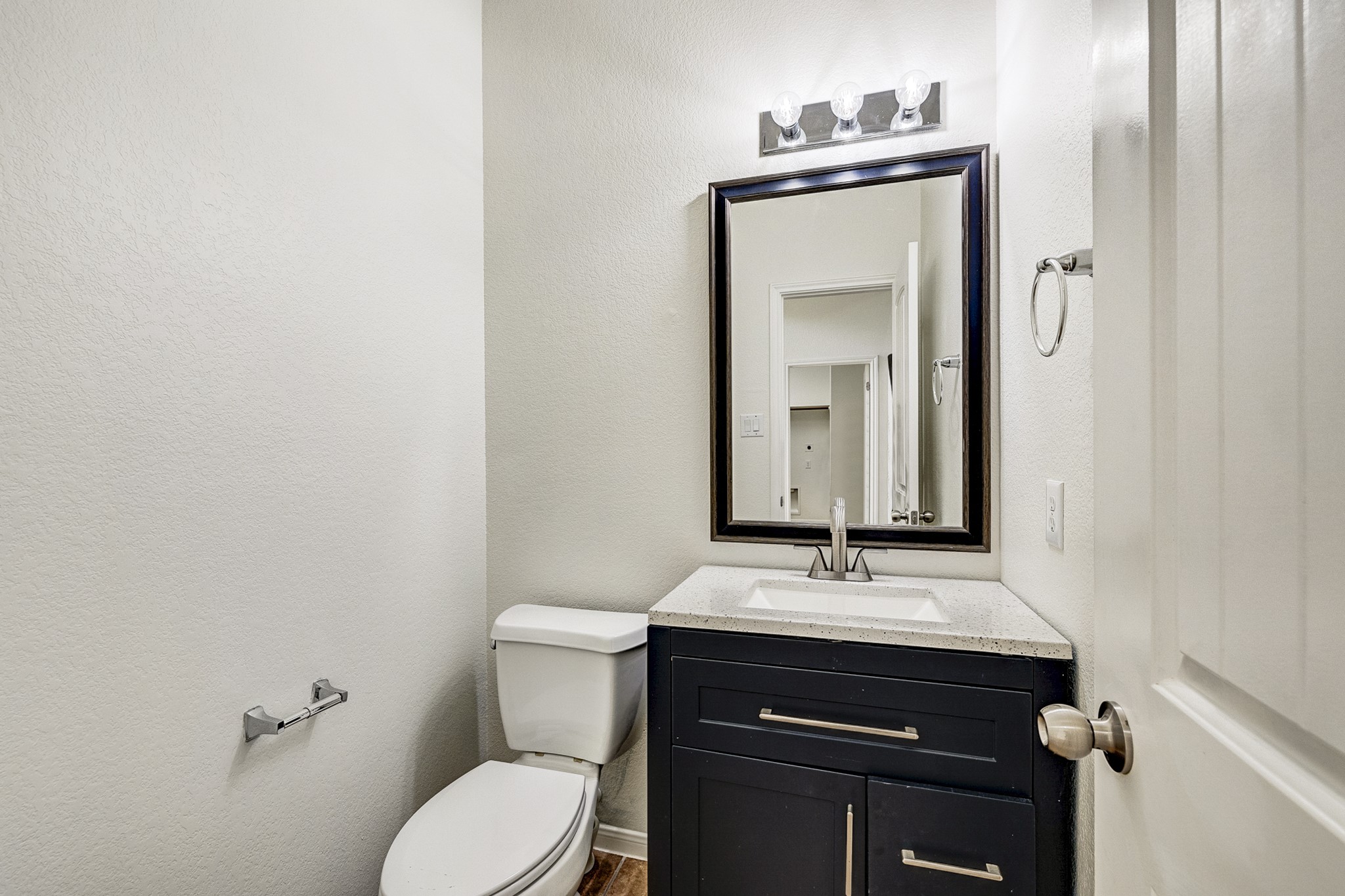 Modern half-bath featuring a sleek vanity with granite countertop, elegant lighting, and a large framed mirror for a touch of sophistication.