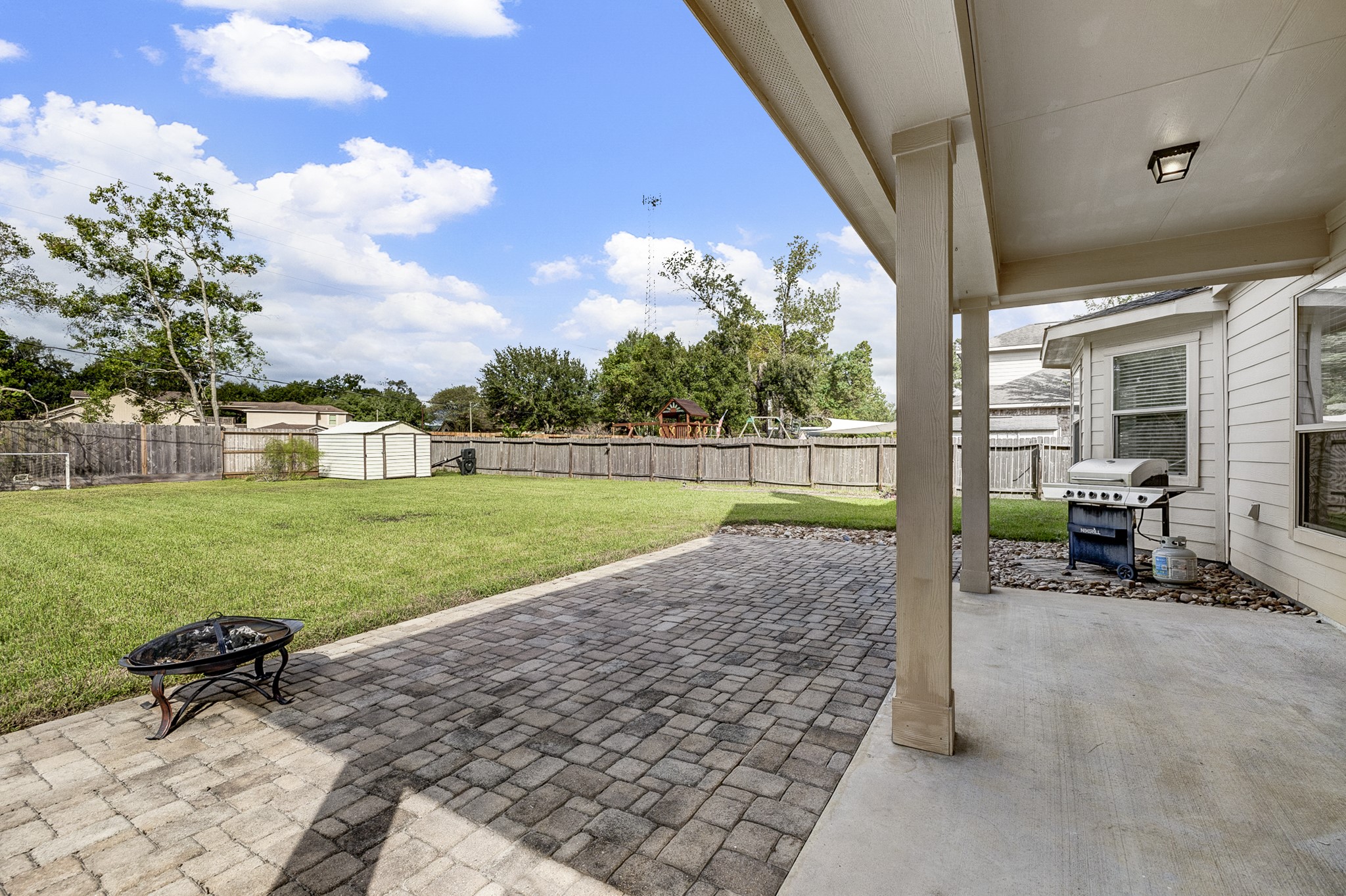 Spacious backyard featuring a covered patio with a grill, perfect for outdoor entertaining, and a large, well-maintained lawn ideal for recreation and relaxation.