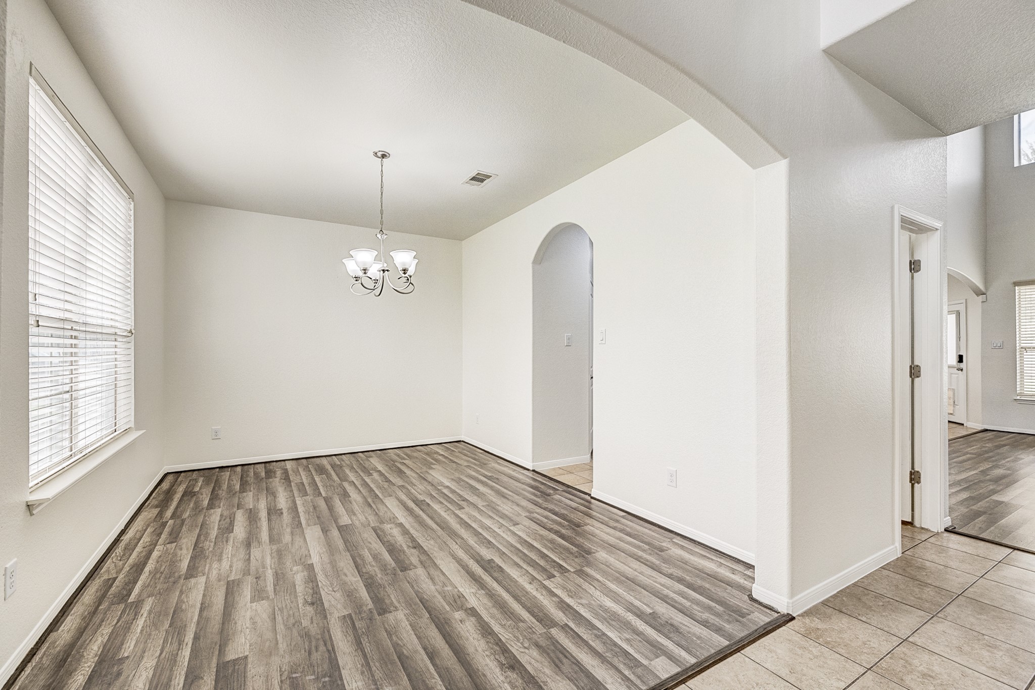 Bright dining area with elegant wood flooring, large windows, and a modern chandelier, seamlessly connected to other living spaces through an arched doorway.