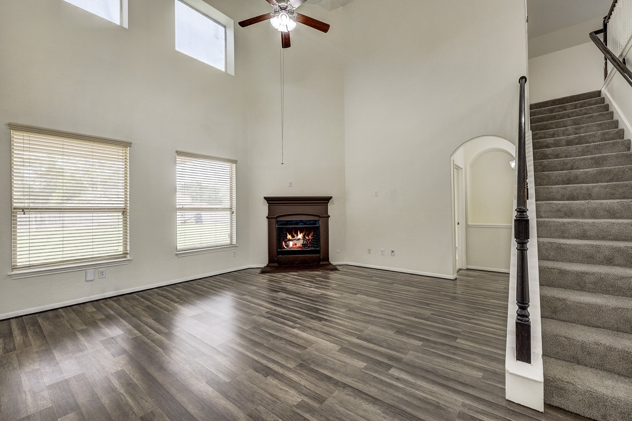 Spacious living area featuring high ceilings, a cozy fireplace, and elegant flooring, complemented by large windows for ample natural light and an open staircase leading to the upper level.