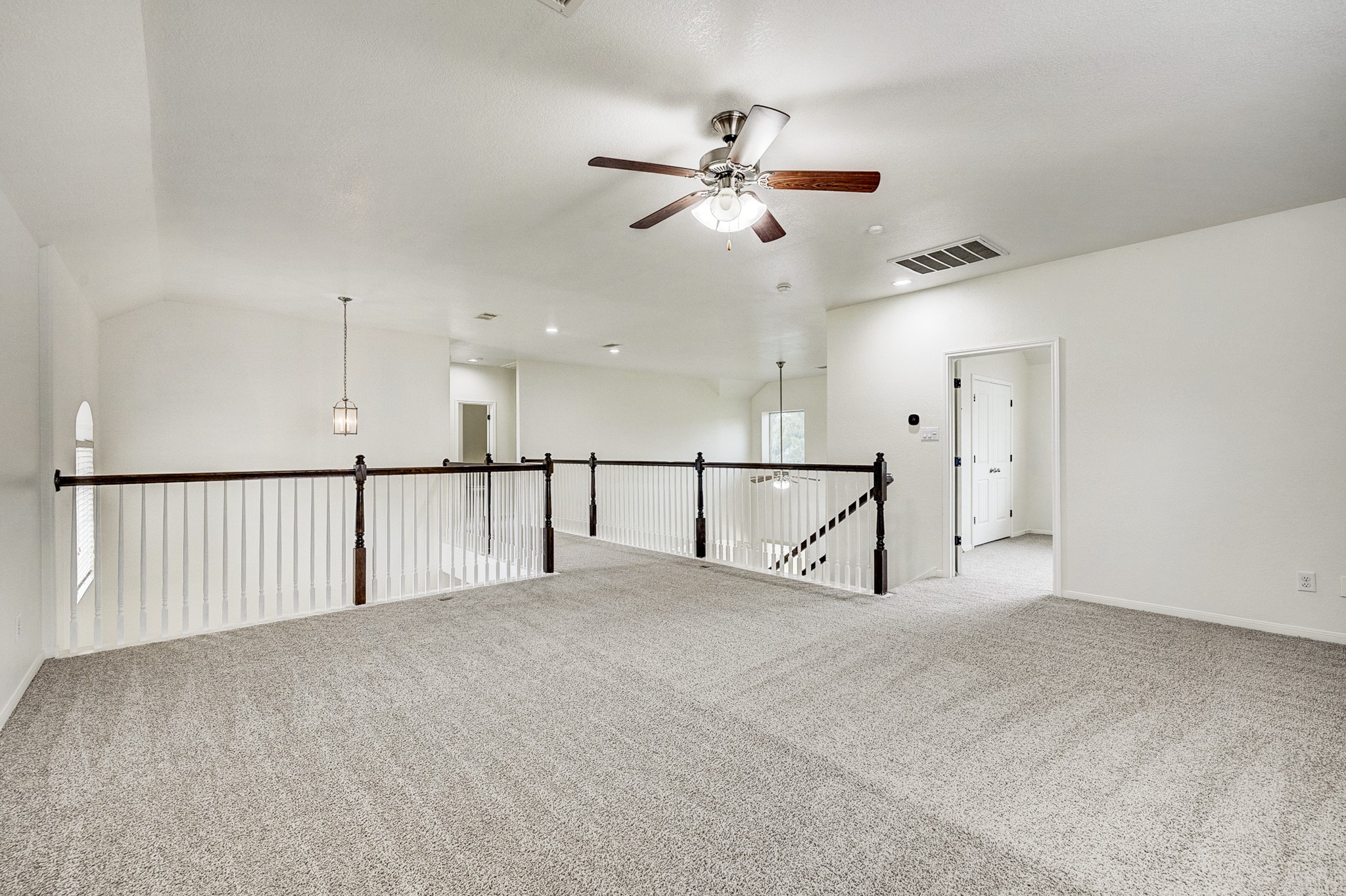 Spacious and bright loft area with plush carpeting, an elegant ceiling fan, and stylish railing overlooking the lower level. Ideal for a cozy lounge or home office setup.