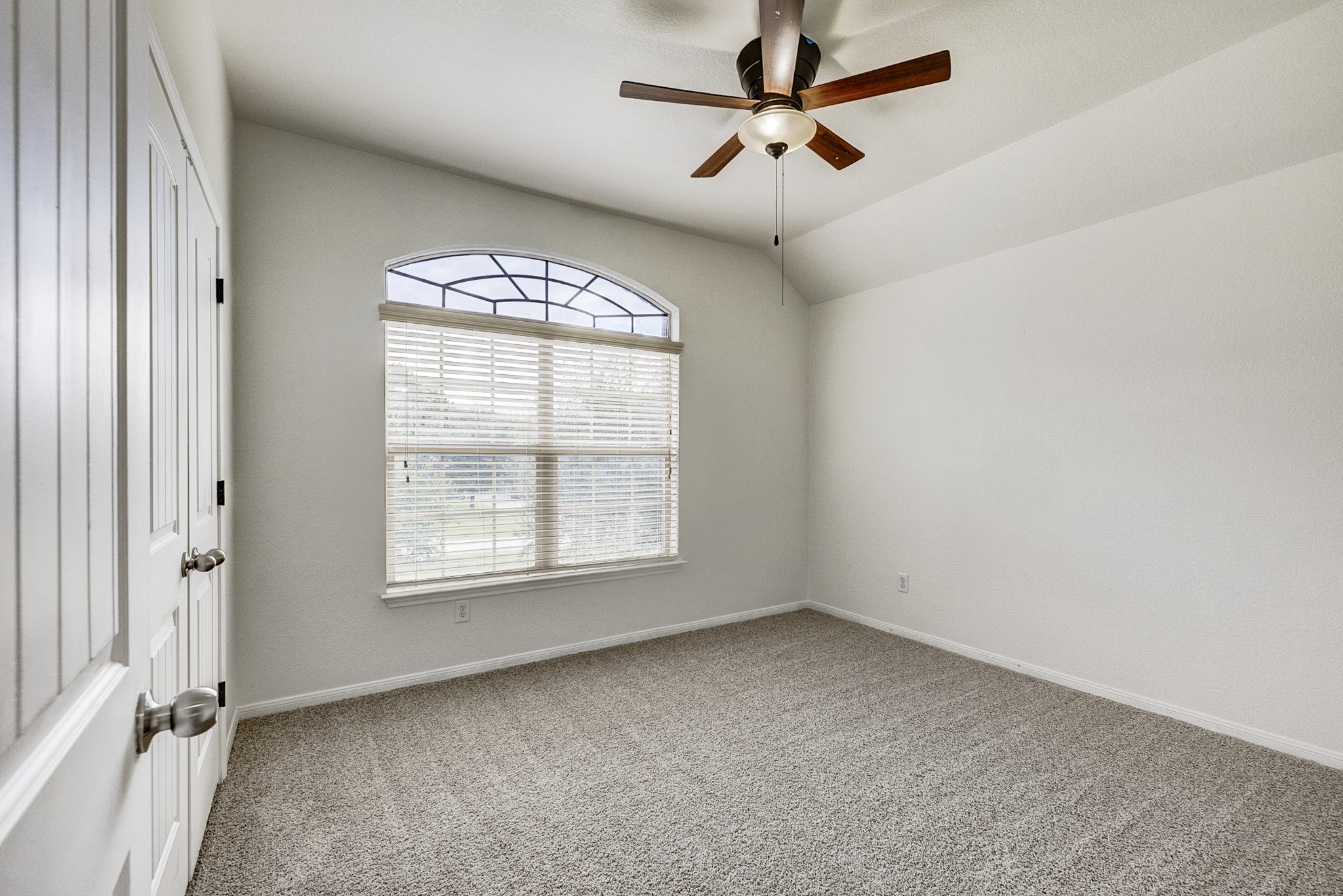 Bright and airy bedroom featuring a large arched window, plush carpeting, and a stylish ceiling fan.