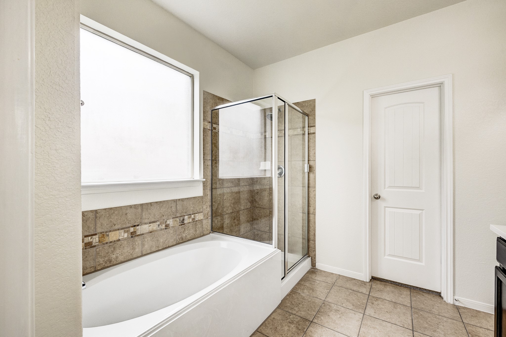 Bright and inviting bathroom featuring a spacious soaking tub, elegant tiled shower, and ample natural light from a large frosted window.