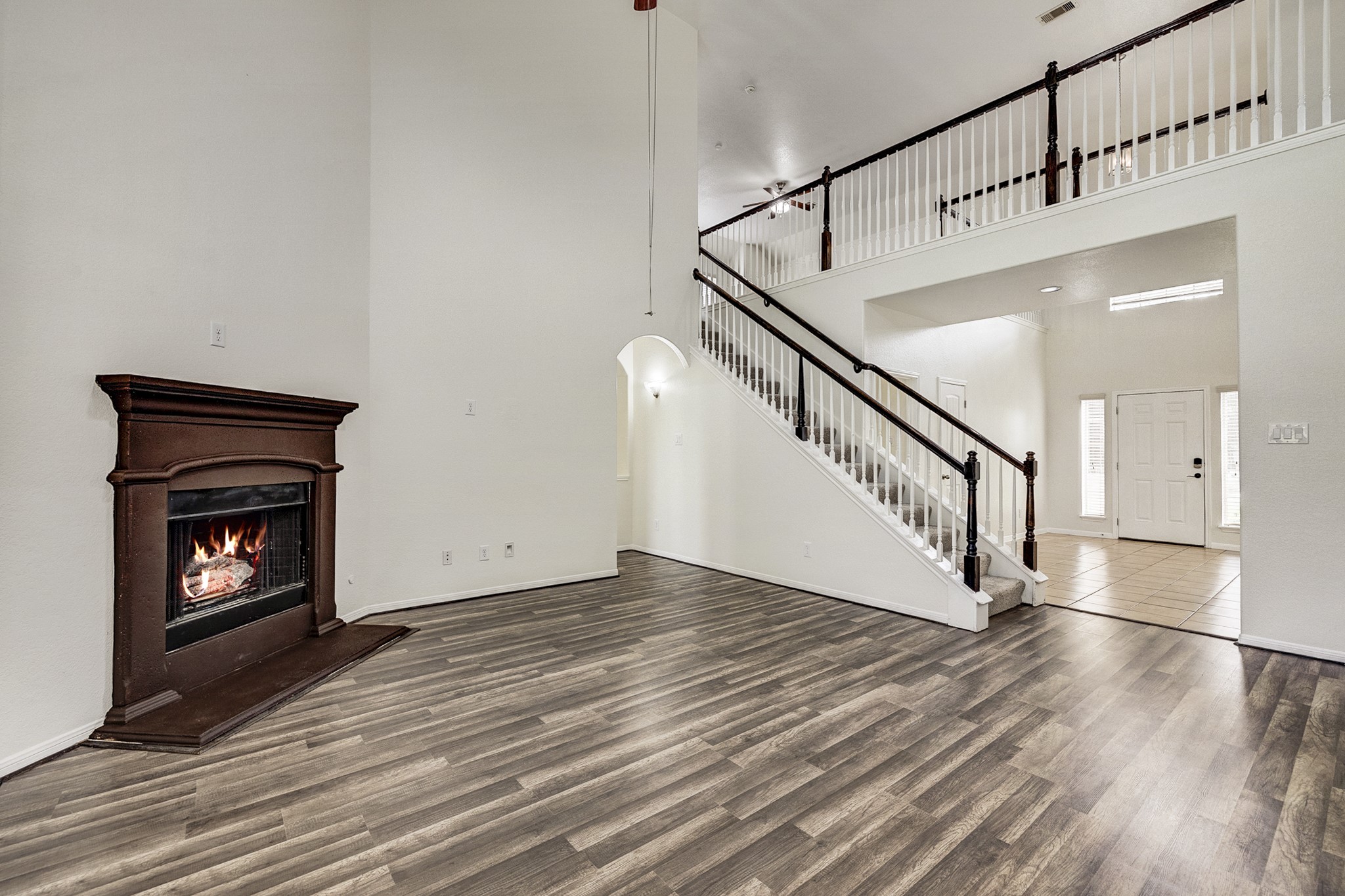 Spacious living area with elegant laminate flooring, a cozy fireplace, and a grand staircase leading to the upper level.