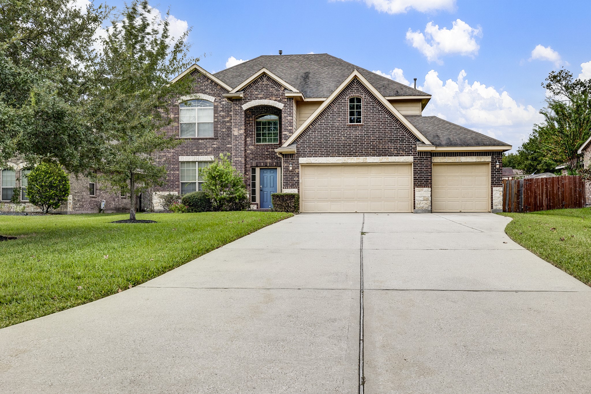 Stunning two-story brick home featuring a spacious three-car garage, manicured lawn, and elegant arched entryway.