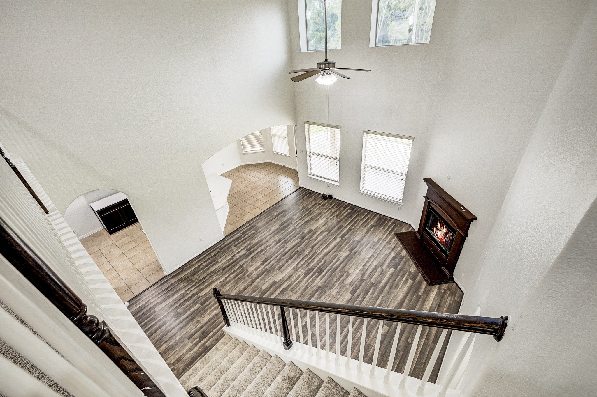Spacious living area with soaring ceilings, abundant natural light from large windows, elegant wood flooring, and a cozy corner fireplace for ultimate comfort.