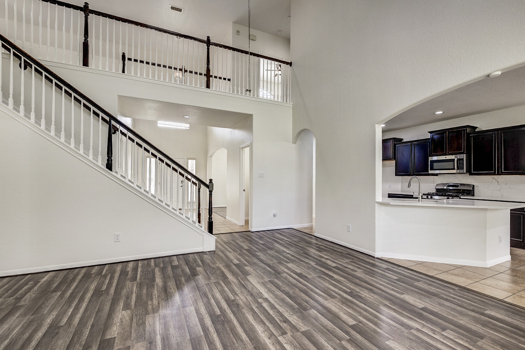 Spacious open-concept living area featuring elegant wood flooring, a dramatic staircase, and a modern kitchen with dark cabinetry and stainless steel appliances.