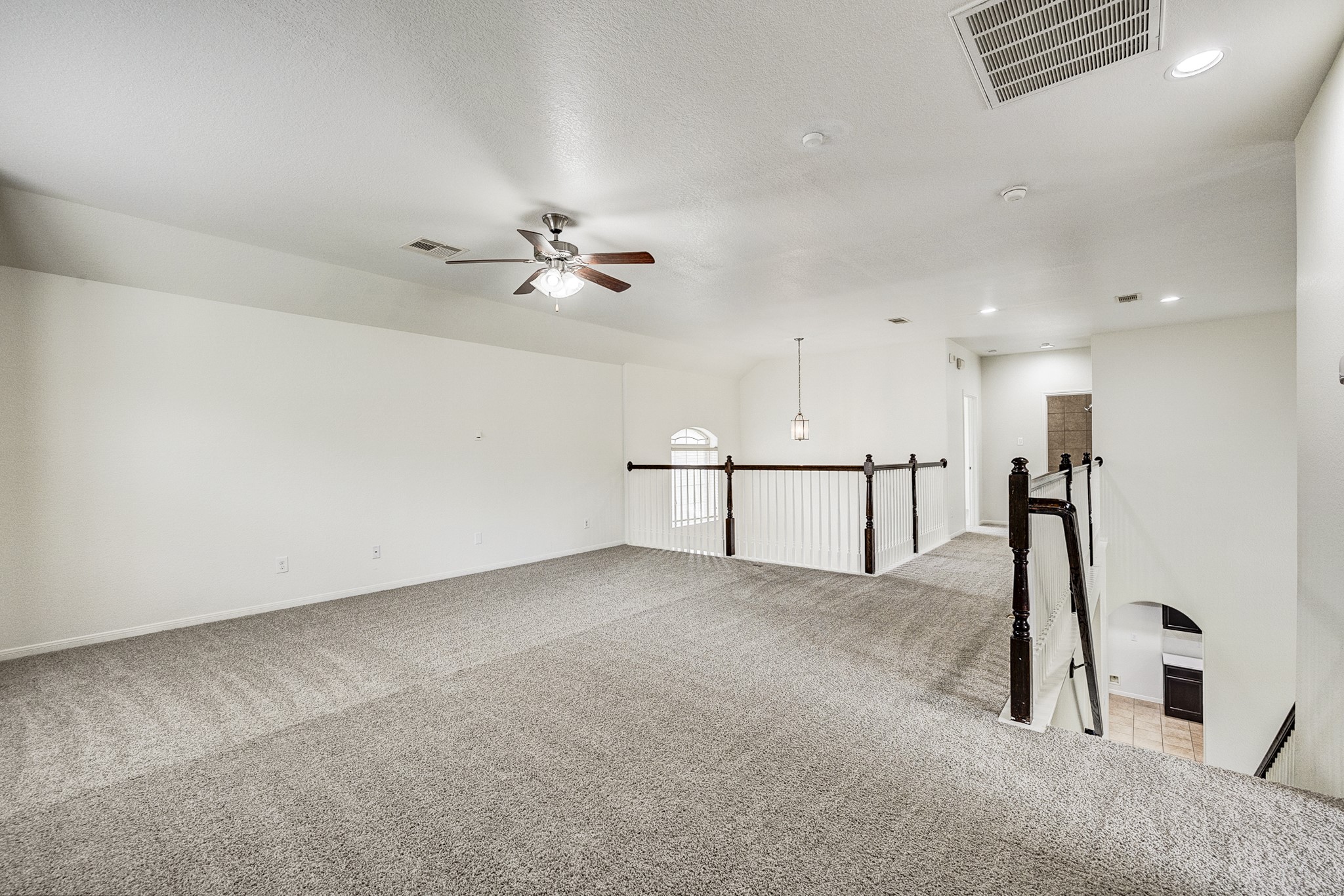 Spacious and airy loft area with plush carpeting, ceiling fan, and elegant railing, perfect for a versatile living space or office.