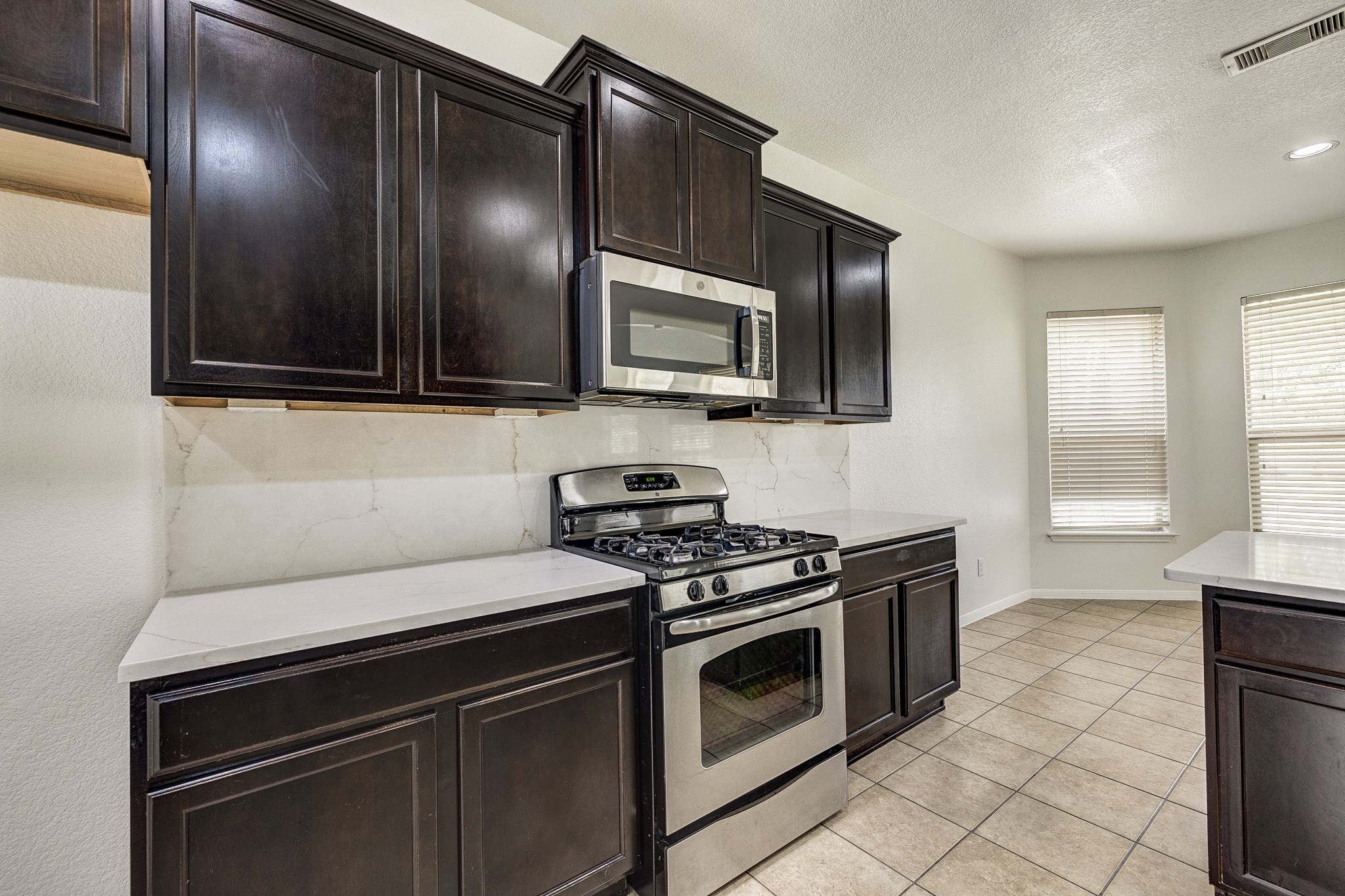 Modern kitchen featuring dark wood cabinets, sleek stainless steel appliances, and a bright dining area with large windows.