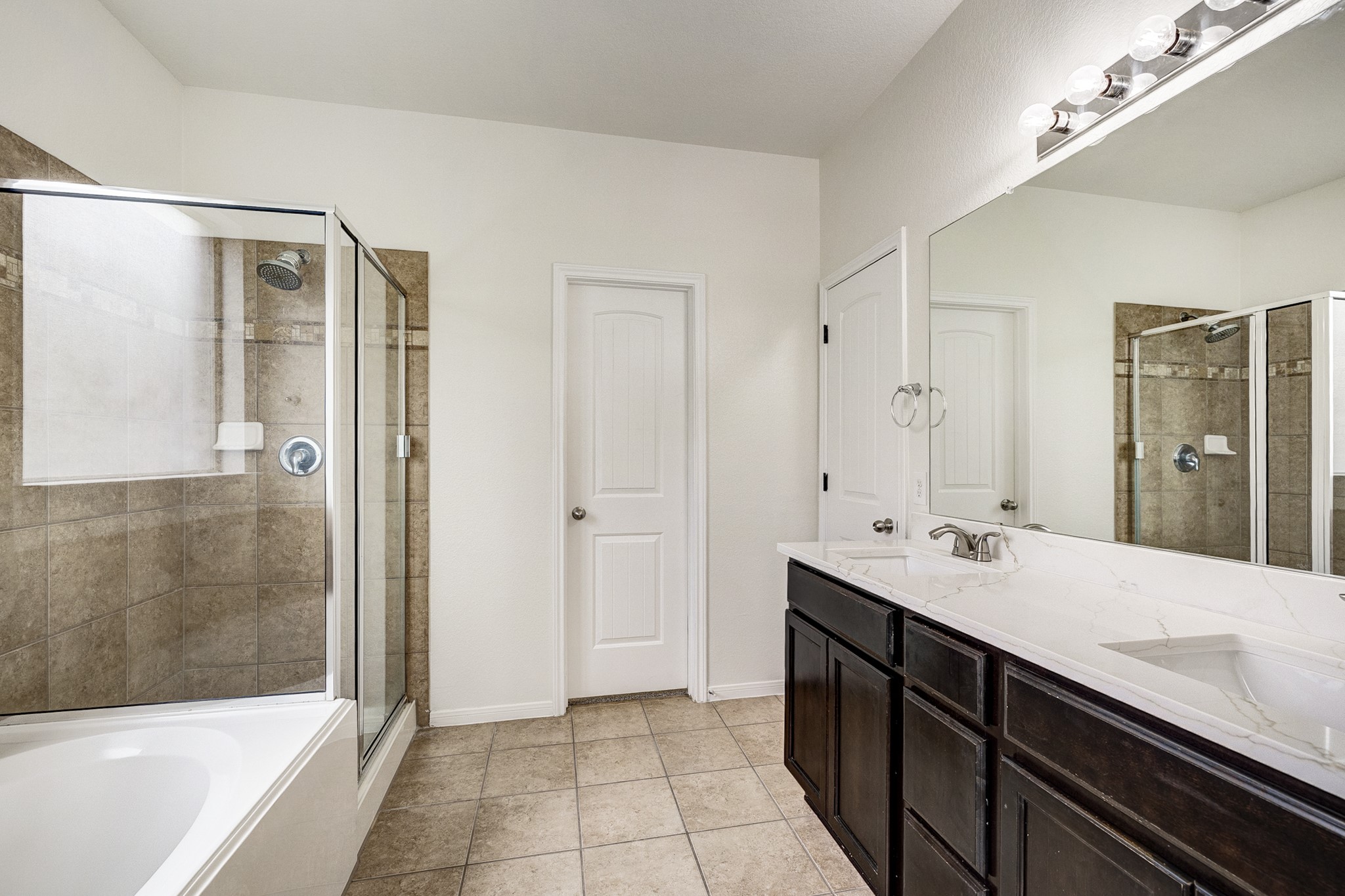 Spacious bathroom featuring a sleek glass-enclosed shower, a luxurious soaking tub, and a modern double vanity with elegant dark cabinetry.