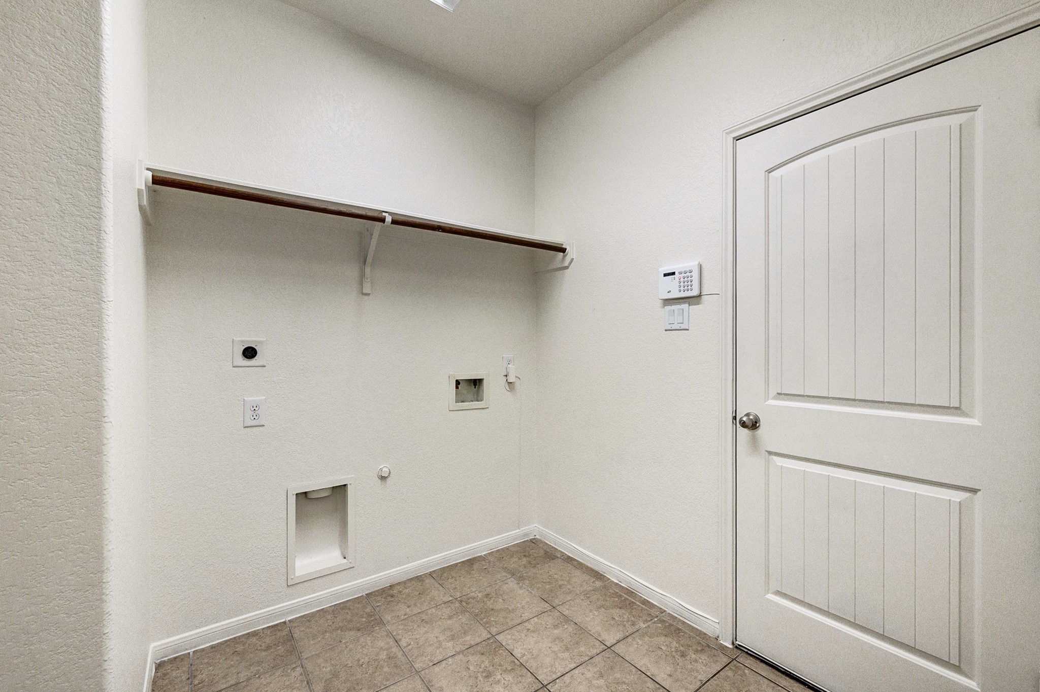 Spacious laundry room with tile flooring, washer and dryer hookups, a convenient shelf for storage, and a secure entry door.