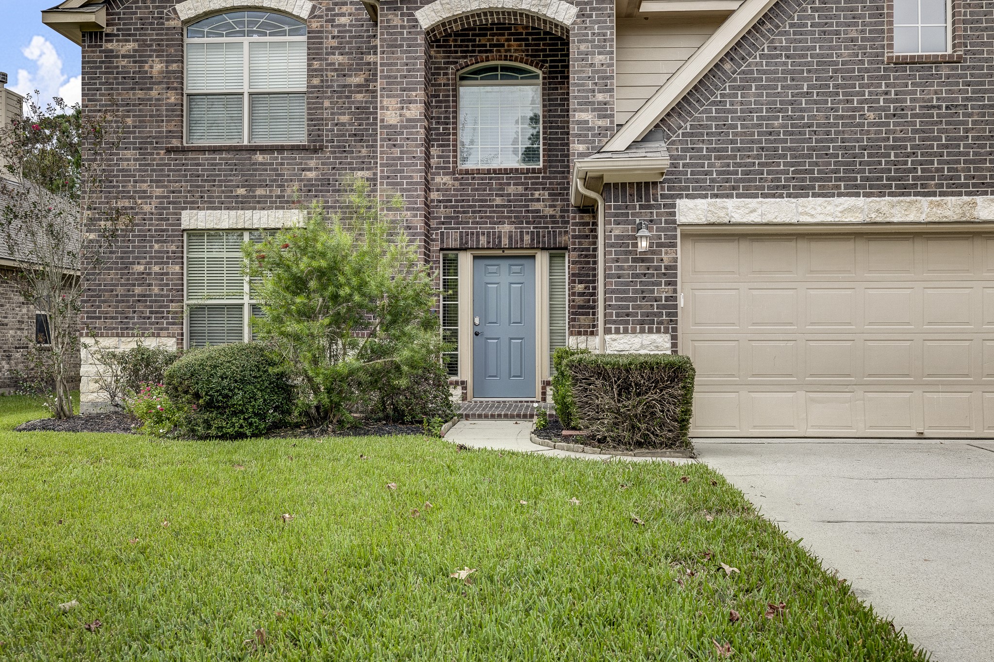 Charming two-story brick home with a welcoming blue front door, complemented by a neatly trimmed lawn and well-maintained shrubs.