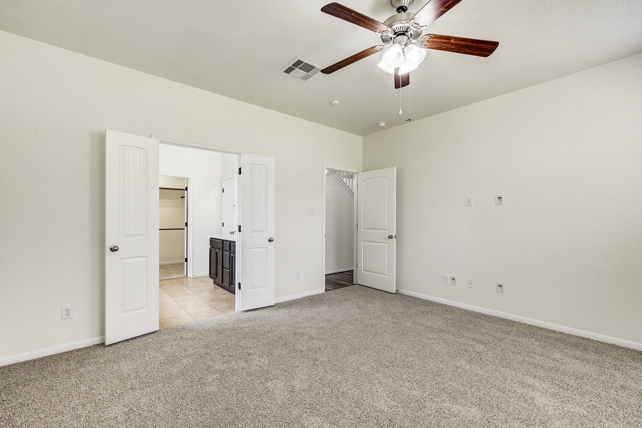 Spacious bedroom with plush carpeting, a ceiling fan, and double doors leading to an en-suite bathroom.