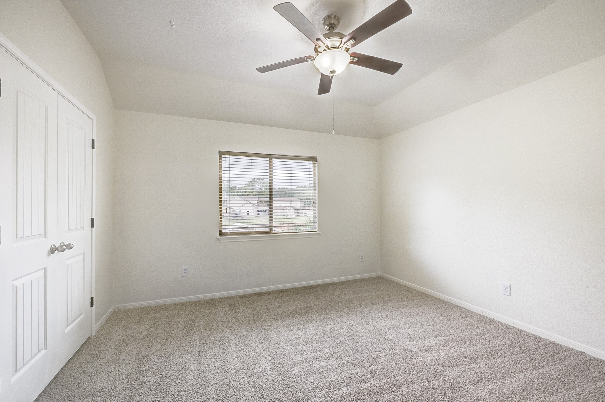 Spacious bedroom with plush carpeting, a ceiling fan, and ample natural light from the window.