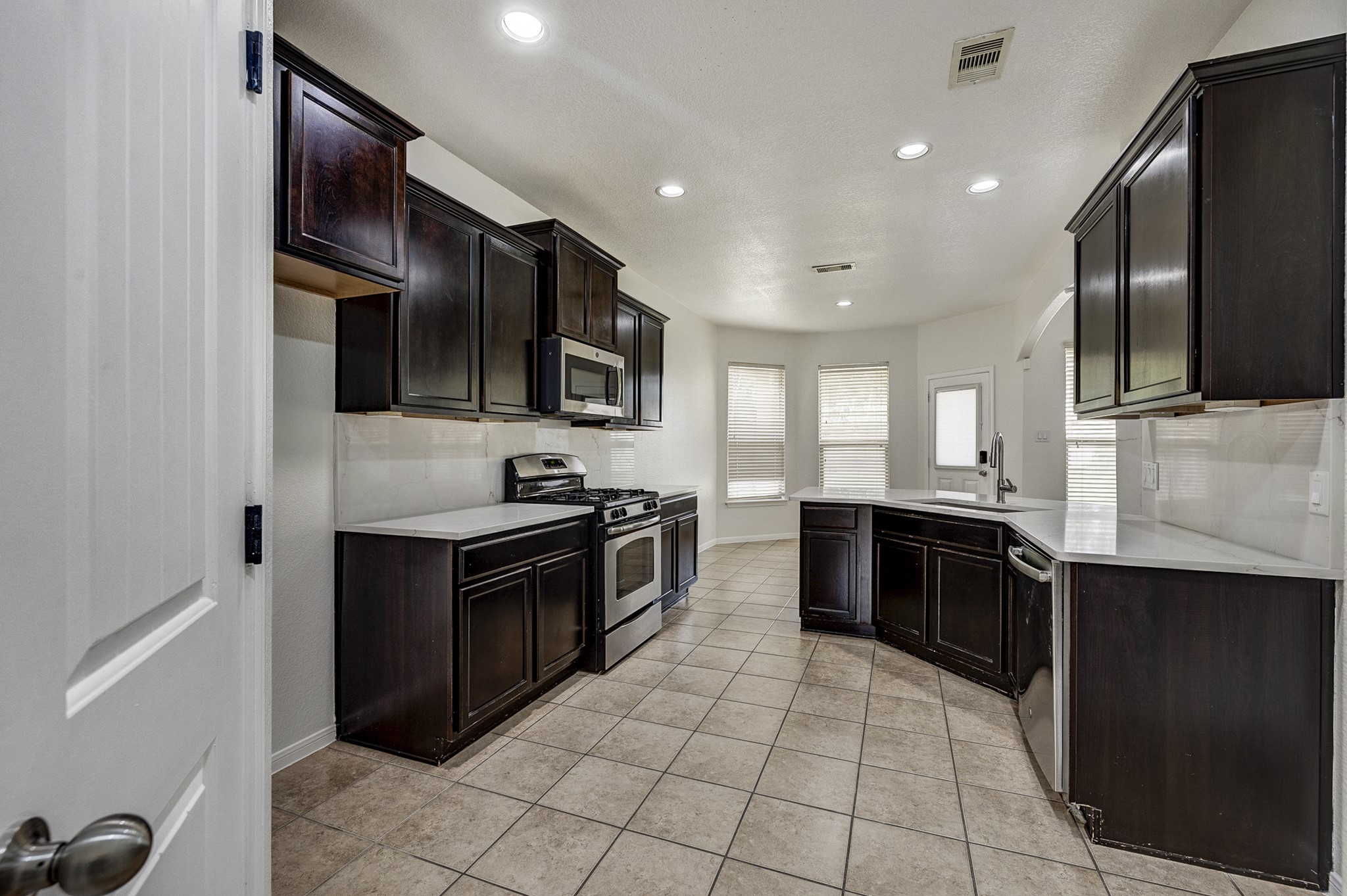 Spacious kitchen with rich dark cabinetry, modern stainless steel appliances, and elegant tiled flooring, complemented by abundant natural light from large windows.
