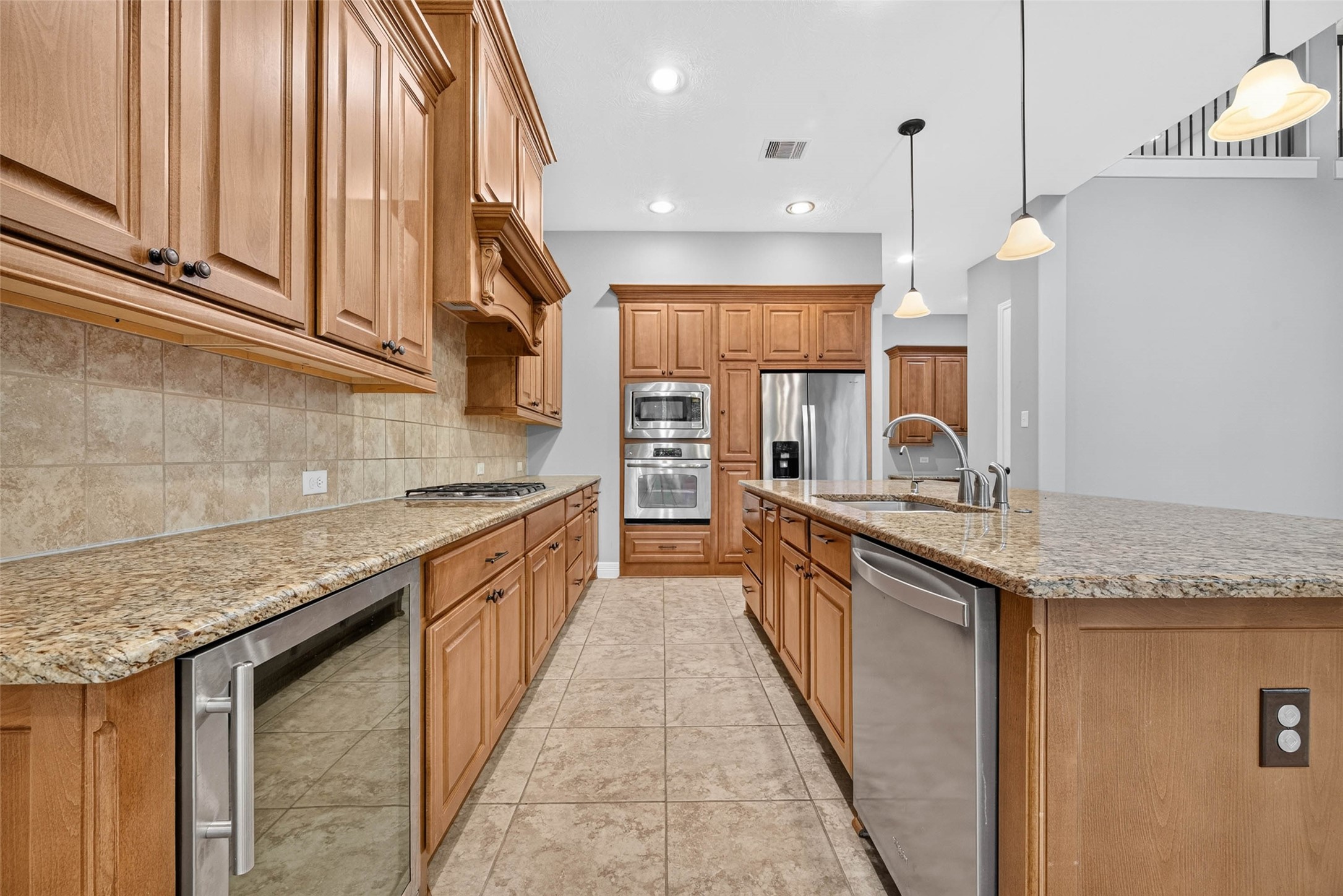 This modern kitchen features an expansive center island with a built-in sink, stainless steel appliances, and a dedicated wine refrigerator