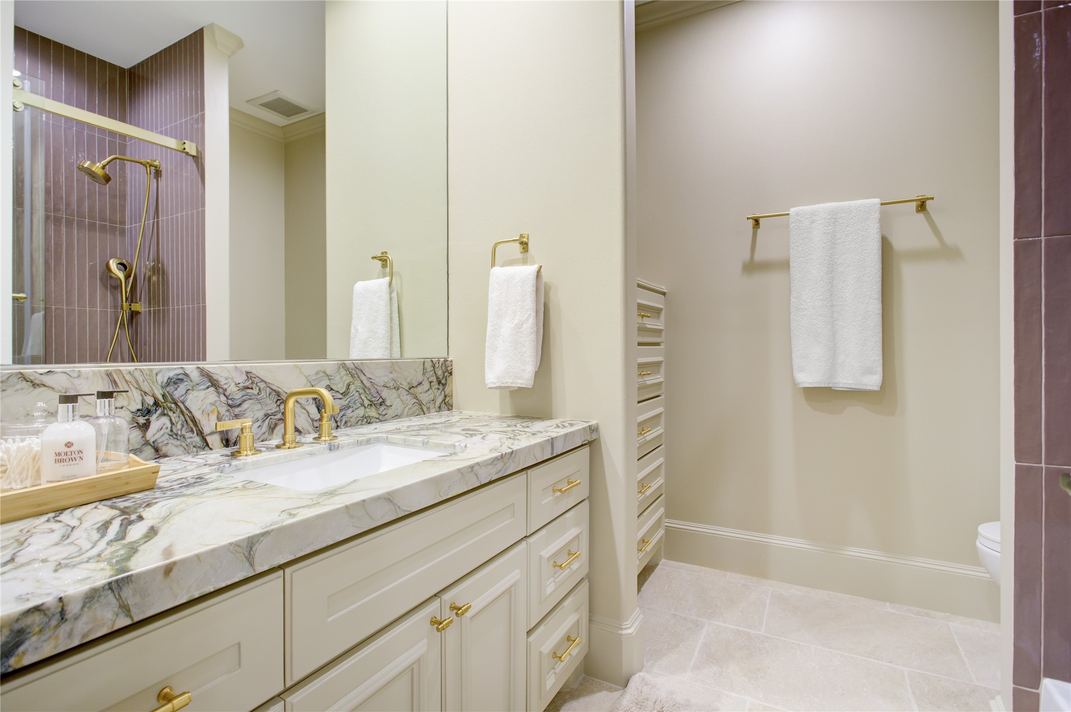 Mauve linear tile, green fusion countertops, and travertine flooring create a distinctive, artfully layered ensuite.