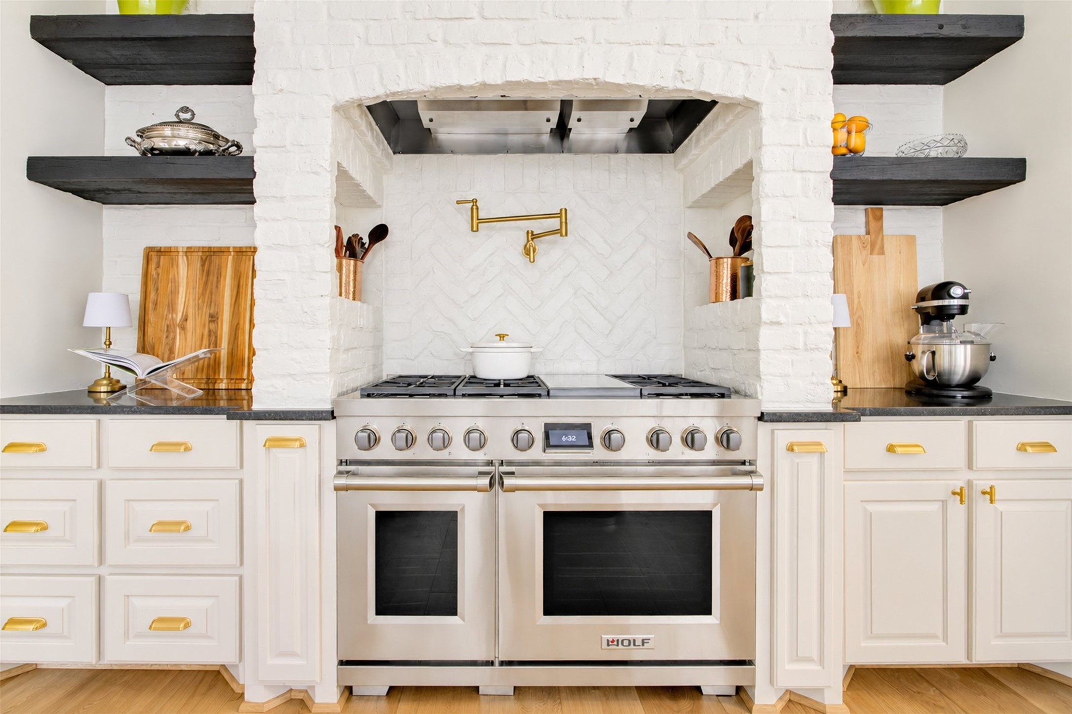 A Wolf professional range with double ovens ancors the herringbone brick cooking alcove, complete with a Kohler brass pot filler.