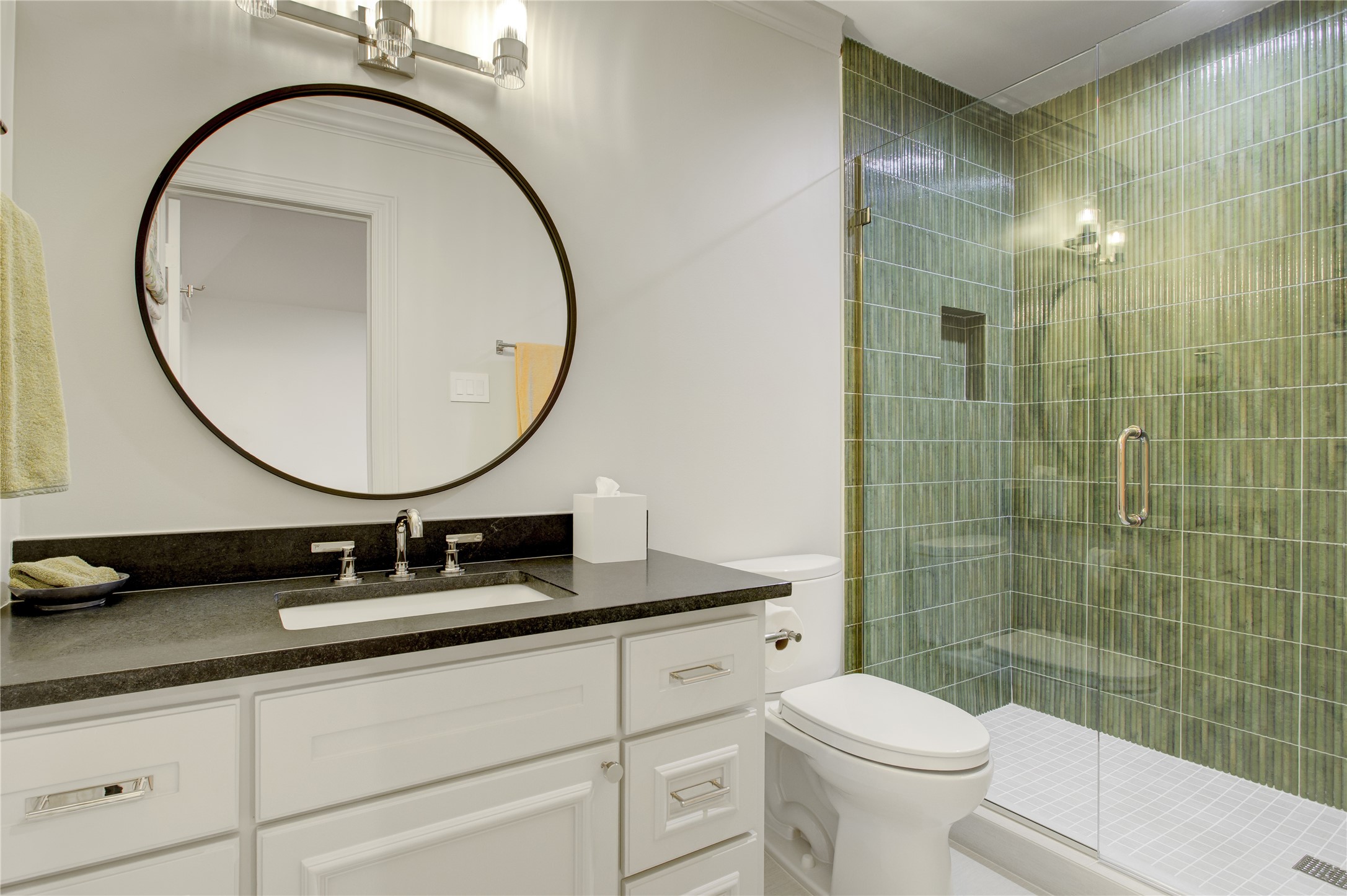 Textured emerald green tile makes a bold statement alongside honed black granite countertops and a spacious walk-in shower.