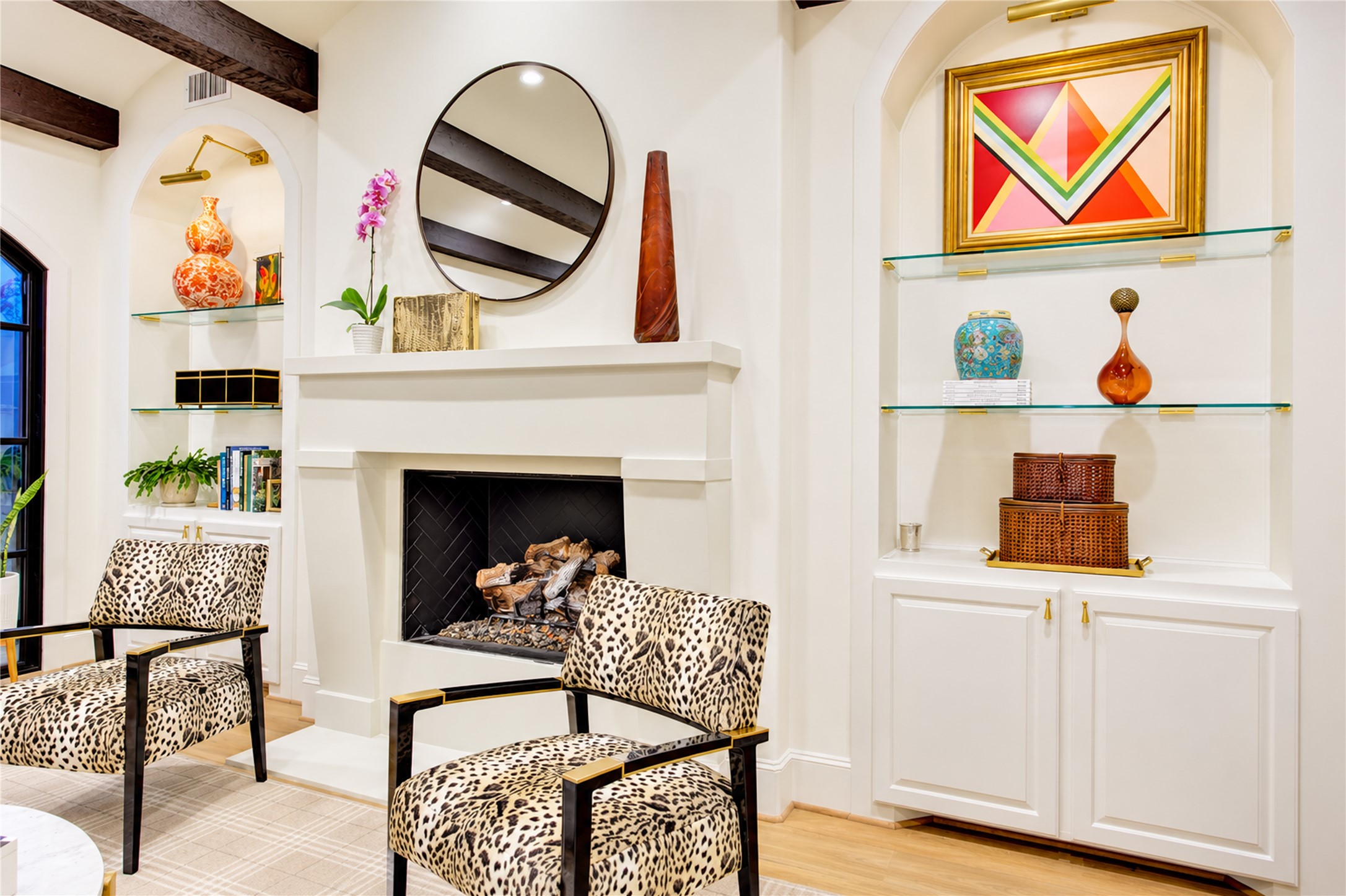 A cast stone gas-log fireplace with a classic mantel anchors the living room, flanked by arched display niches with floating glass shelves.