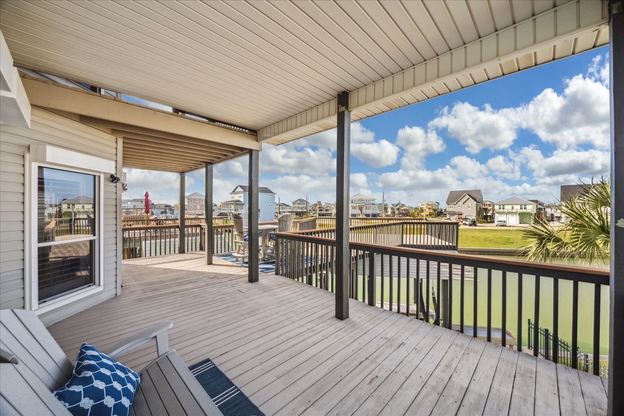 A spacious, covered deck overlooking a serene waterfront with views of neighboring homes. Ideal for relaxing and enjoying the outdoors.