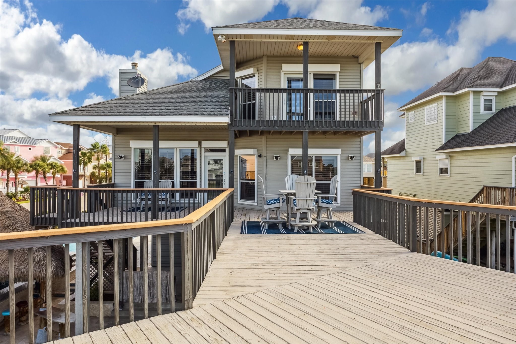 This inviting home features a spacious wooden deck with ample seating, perfect for entertaining. The exterior offers a modern design with a two-story layout and a charming balcony. Ideal for enjoying sunny days.