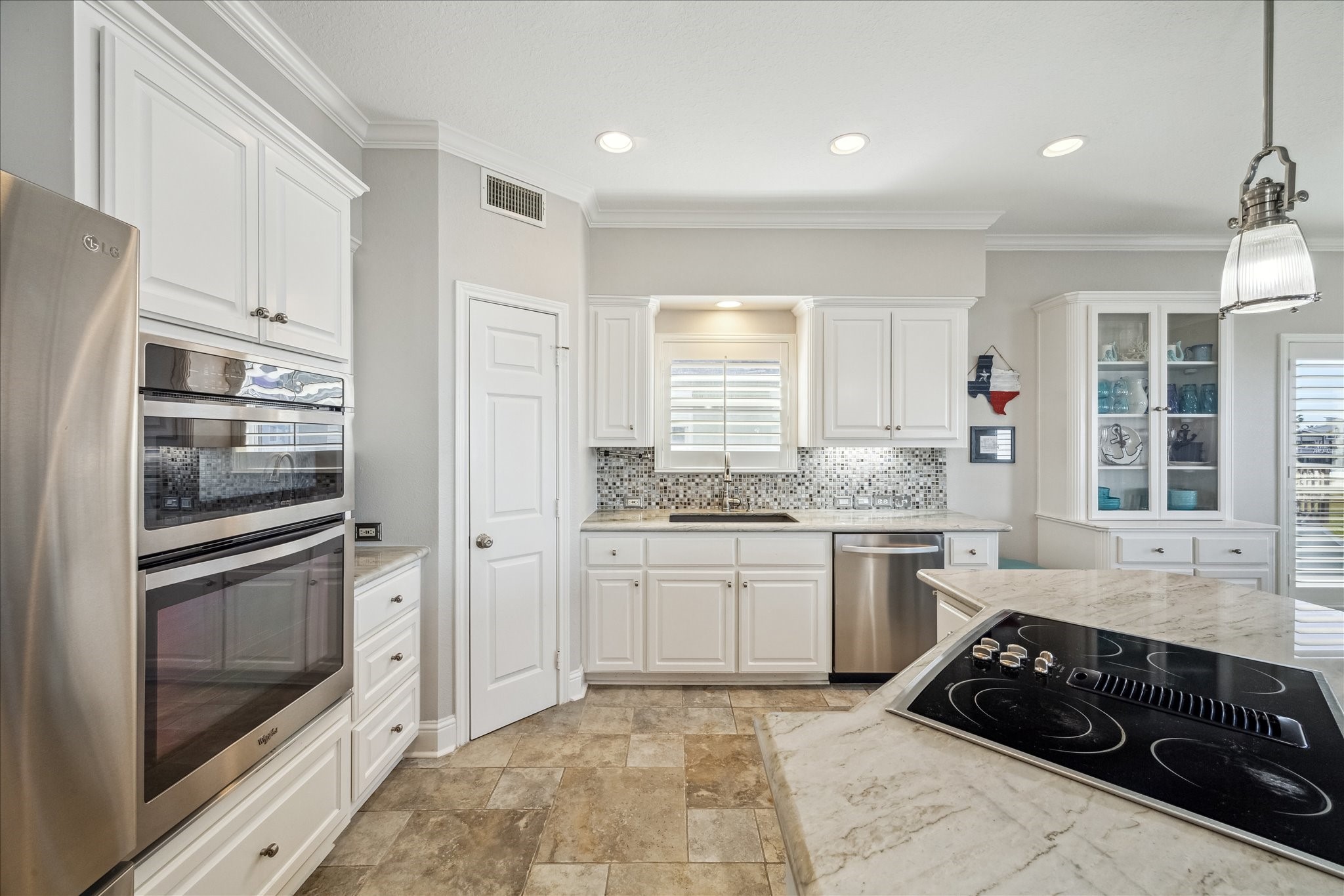 This kitchen features  a built-in oven, a sleek cooktop on a marble island, and ample natural light.