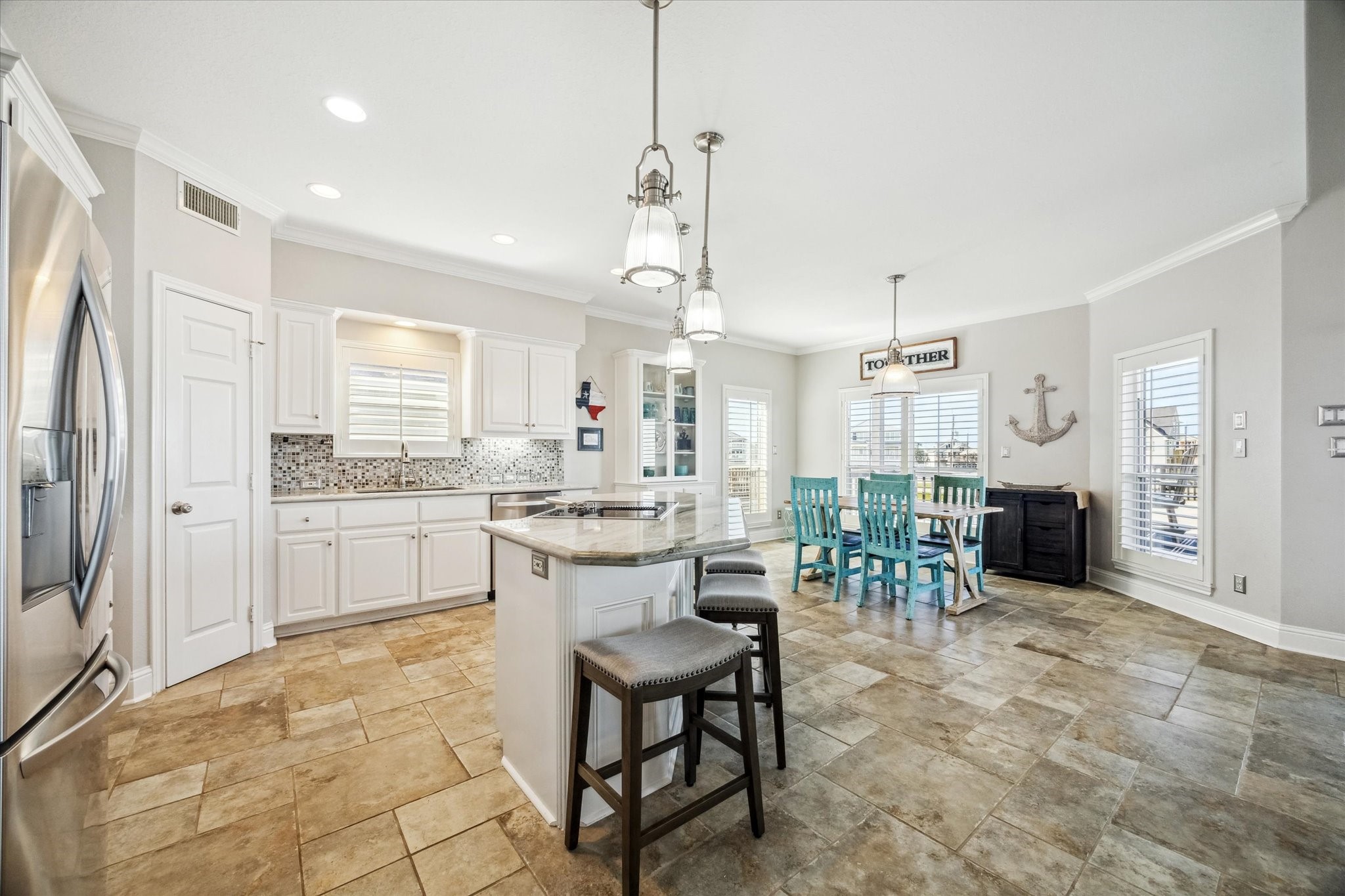 This spacious kitchen and dining area features modern appliances, an island with seating, and ample natural light. The space boasts a coastal vibe