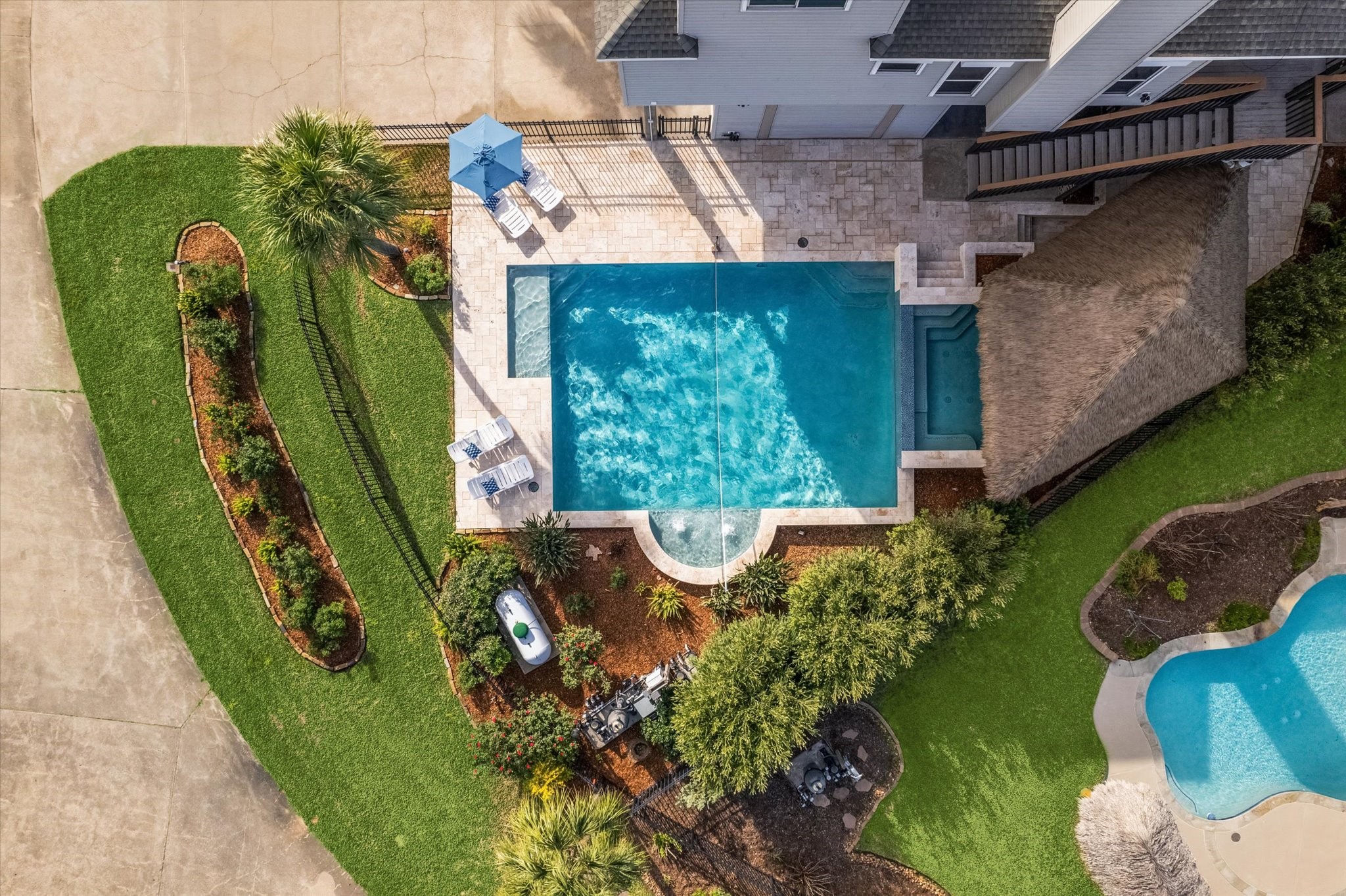 This  well-maintained backyard features a large rectangular pool with a spa, surrounded by a stone patio. There's a shaded area with seating and lush landscaping, creating an inviting space for relaxation and entertainment.