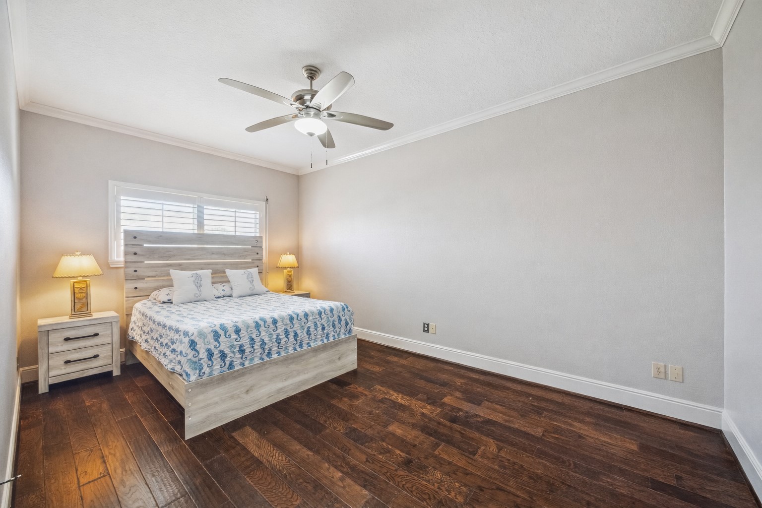 This secondary  bedroom features hardwood floors, a modern ceiling fan, and soft lighting. Neutral walls create a relaxing atmosphere.