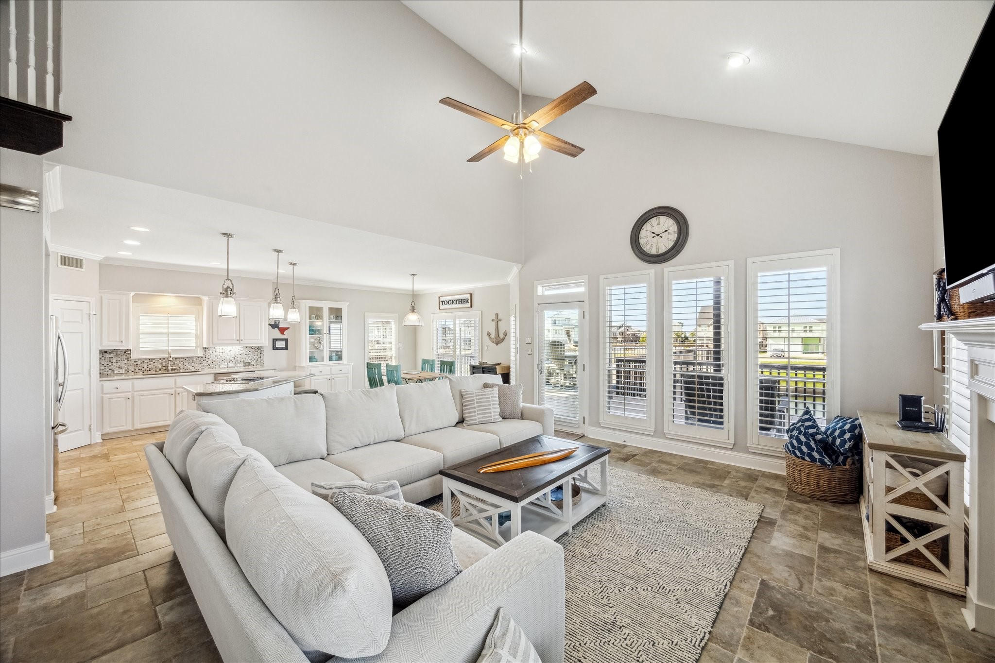 This spacious living area features high ceilings, abundant natural light from large windows, and an open layout leading to a modern kitchen. The cozy seating area is complemented by neutral tones and a fireplace, creating a welcoming atmosphere ideal for family gatherings.