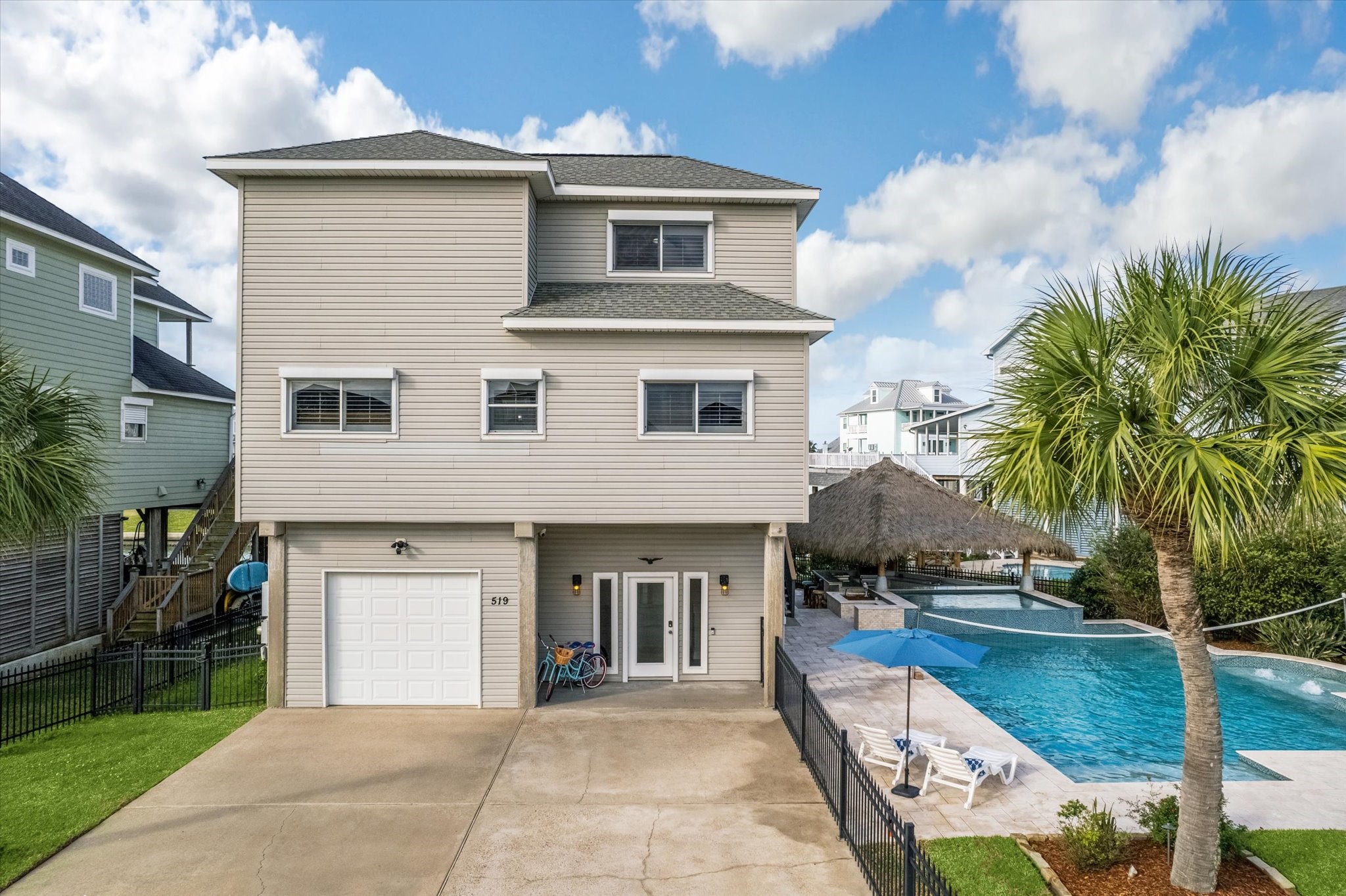 This modern, elevated home features a spacious driveway, a garage, and a luxurious entertaining space with a large pool and patio area. The property is accented by palm trees, offering a tropical feel. This modern, elevated home features a spacious driveway, a garage, and a luxurious entertaining space with a large pool and patio area. The property is accented by palm trees, offering a tropical feel.