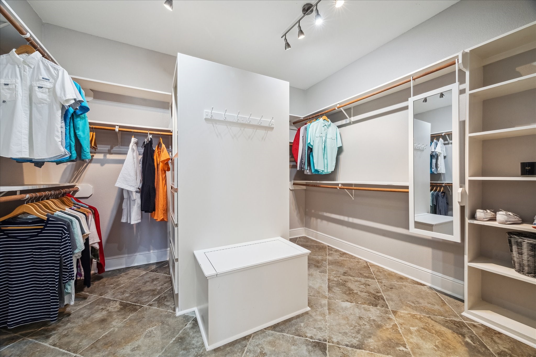 This spacious walk-in closet features ample hanging space, built-in shelves, and a central island with seating. It's well-lit with modern track lighting and has tiled flooring for a sleek, functional look. Ideal for organizing and displaying your wardrobe.