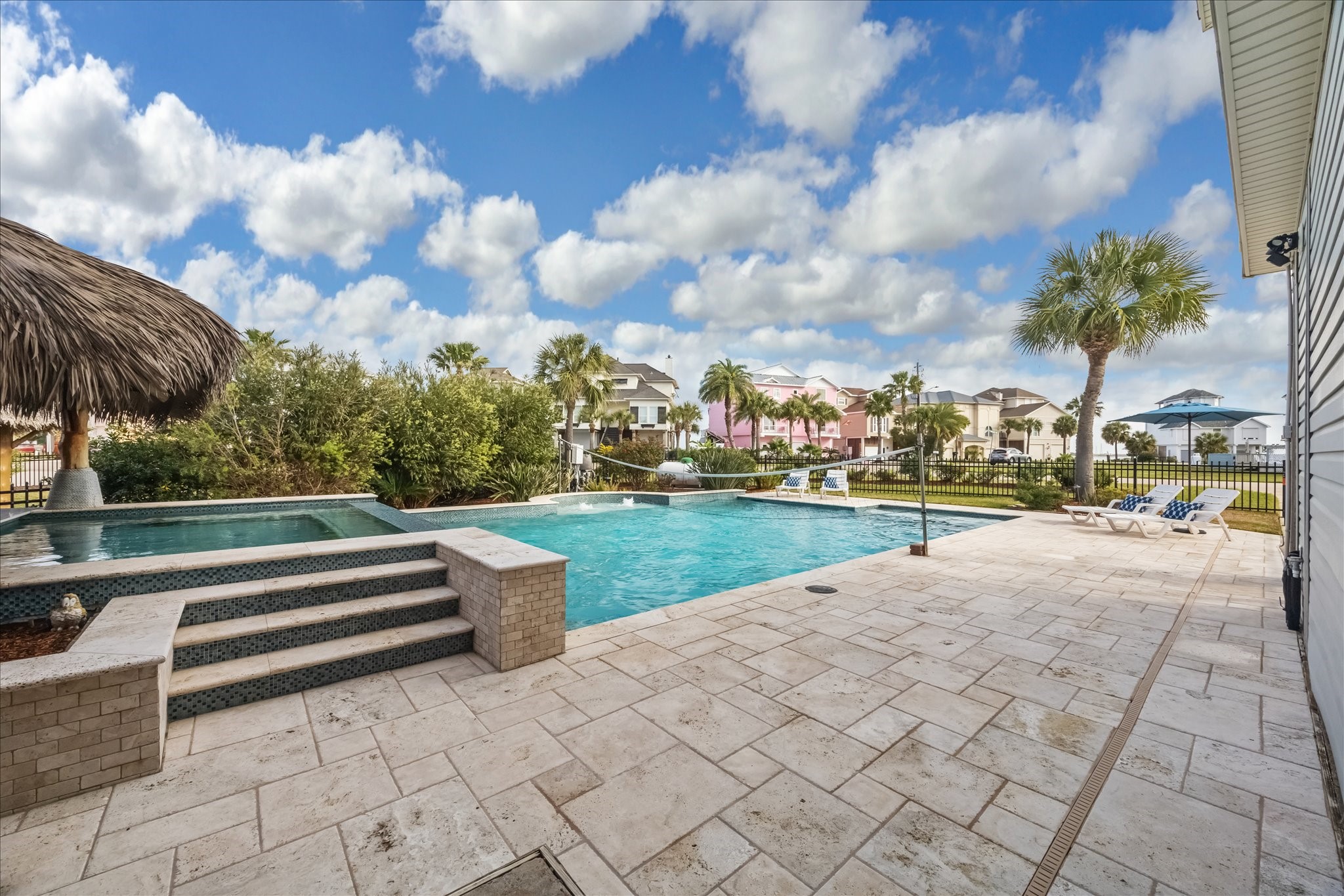 Luxurious pool, a stone-tiled deck, and a palapa. It features lush greenery, palm trees, and a view of colorful neighboring houses, creating a tropical oasis feel. Luxurious pool, a stone-tiled deck, and a palapa. It features lush greenery, palm trees, and a view of colorful neighboring houses, creating a tropical oasis feel.