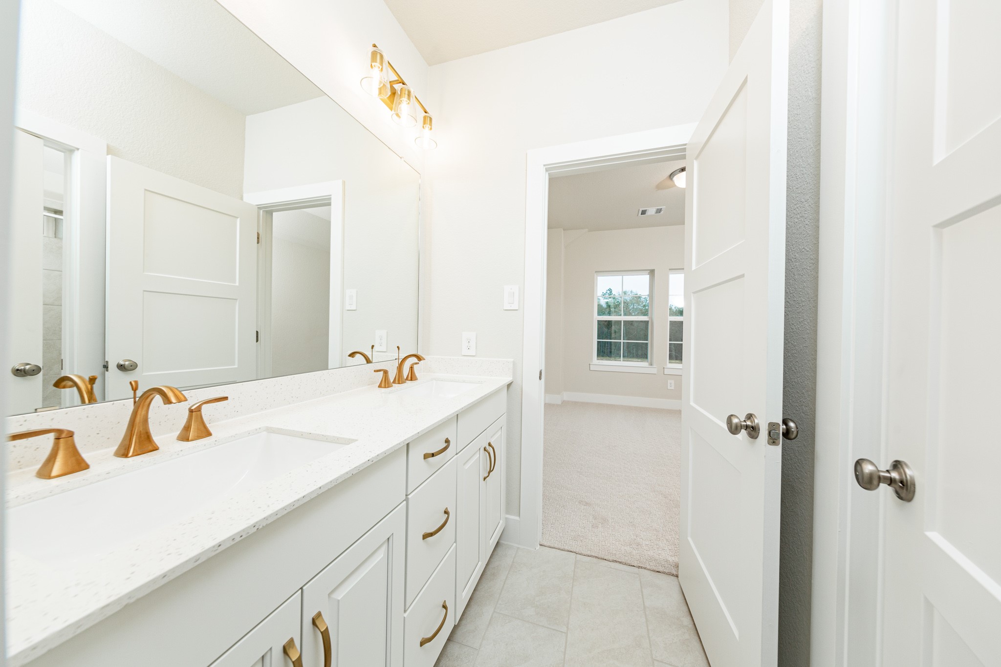 This well-appointed secondary bathroom offers exceptional functionality with stained white cabinetry and white countertops with dual undermount sinks. Sleek, brushed gold fixtures and hardware as well as the chic light fixture complements this space. NOTE: Bathroom has access from 2 secondary bedrooms.