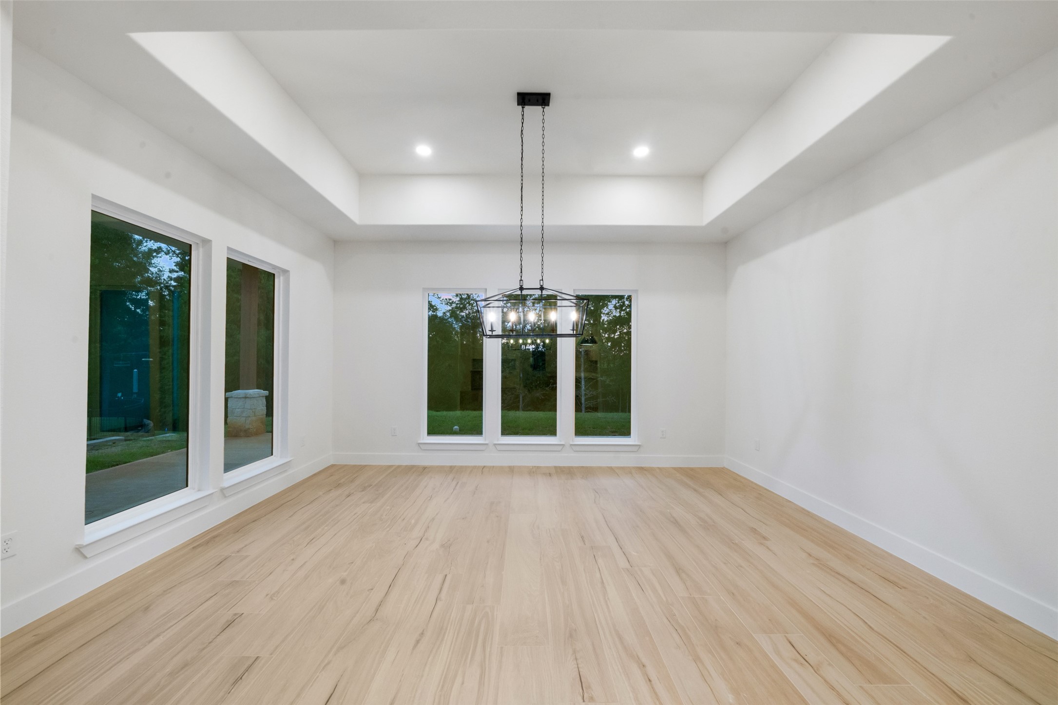 Elegant dining room featuring a beautiful tray ceiling, statement chandelier, and expansive windows overlooking the backyard. Generous proportions provide an exceptional setting for memorable gatherings and formal entertaining.