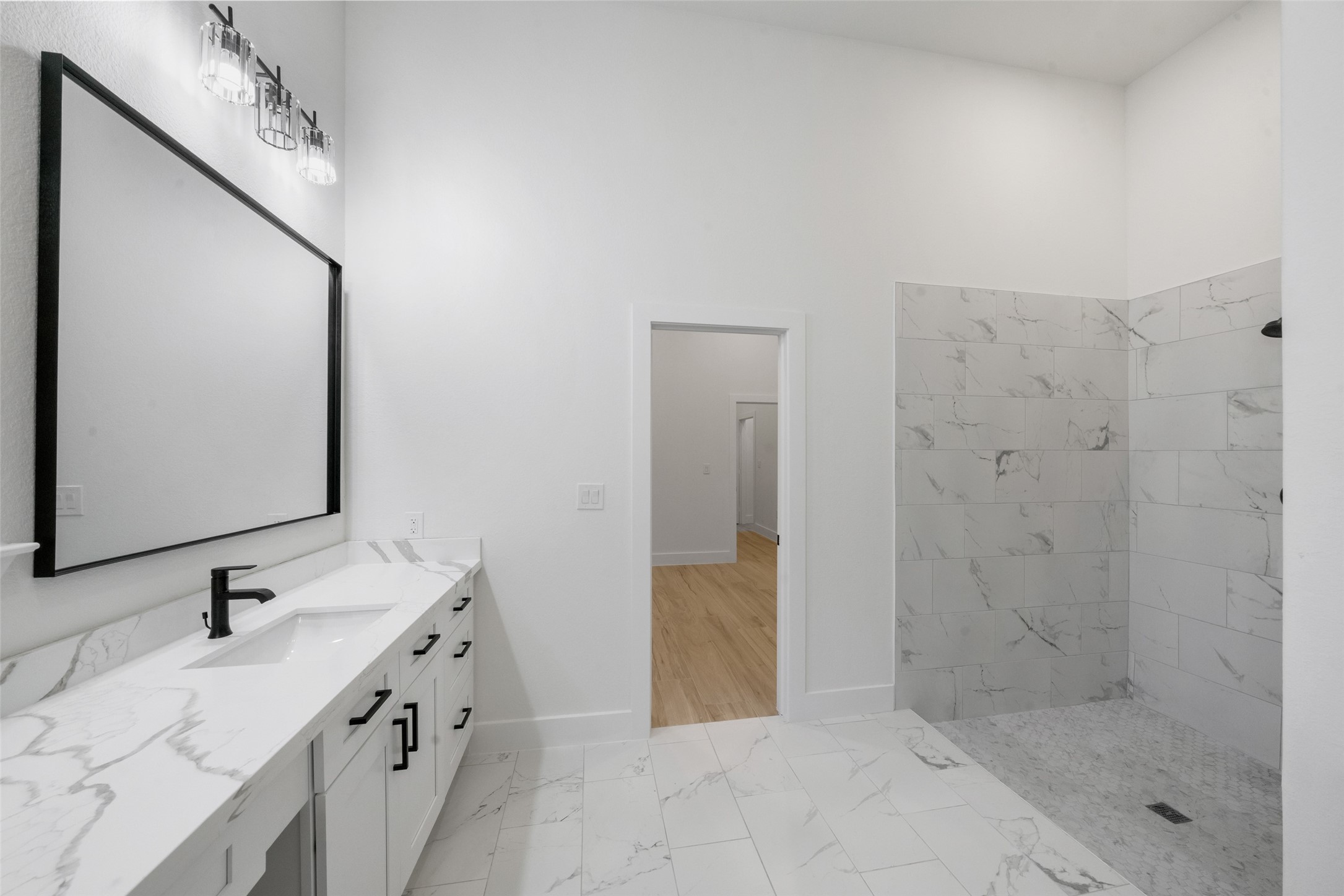 Elegantly designed bathroom showcasing a spacious vanity with marble-look countertops, contemporary black fixtures, and a large framed mirror. Beautifully tiled walk-in shower and sophisticated finishes create a luxurious, spa-inspired retreat.