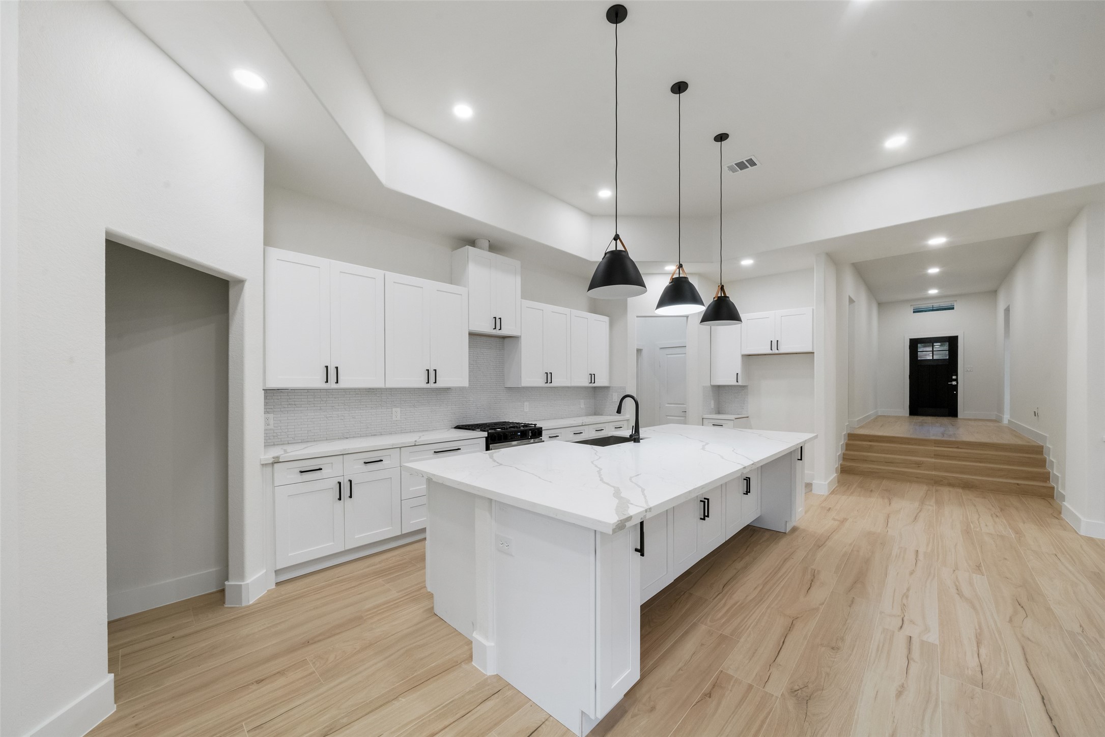 Stunning custom kitchen featuring an oversized island with beautiful marble-look countertops, elegant white cabinetry, sleek black hardware, and designer pendant lighting. A spacious layout and abundant cabinetry create the perfect combination of style and functionality.