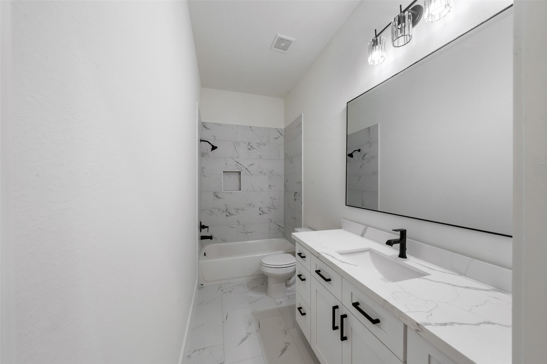 Beautifully finished bathroom featuring marble-look tile, a spacious vanity with sleek black hardware, and contemporary lighting. The shower and tub combination includes elegant tile surrounds and a convenient built-in niche.