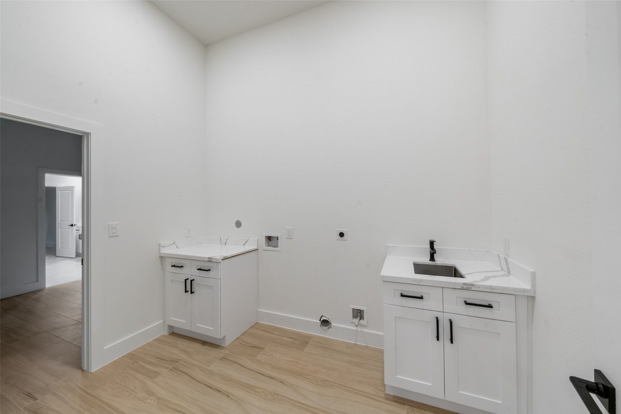 Generously sized laundry room featuring custom white cabinetry, marble-look countertops, a stainless steel utility sink, and sleek black fixtures. Thoughtfully designed with ample workspace, storage, and room for laundry appliances to make everyday tasks effortless.