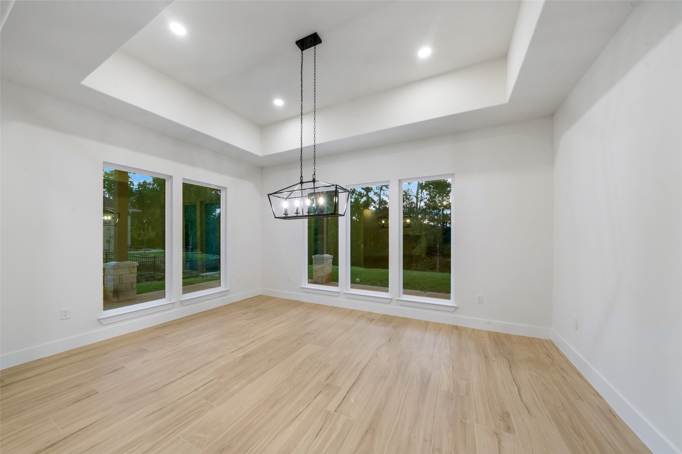 Elegant formal dining room featuring a distinctive tray ceiling, statement chandelier, and expansive windows overlooking the beautifully wooded backyard. Generous proportions and abundant natural light create an inviting setting for intimate dinners or grand entertaining.