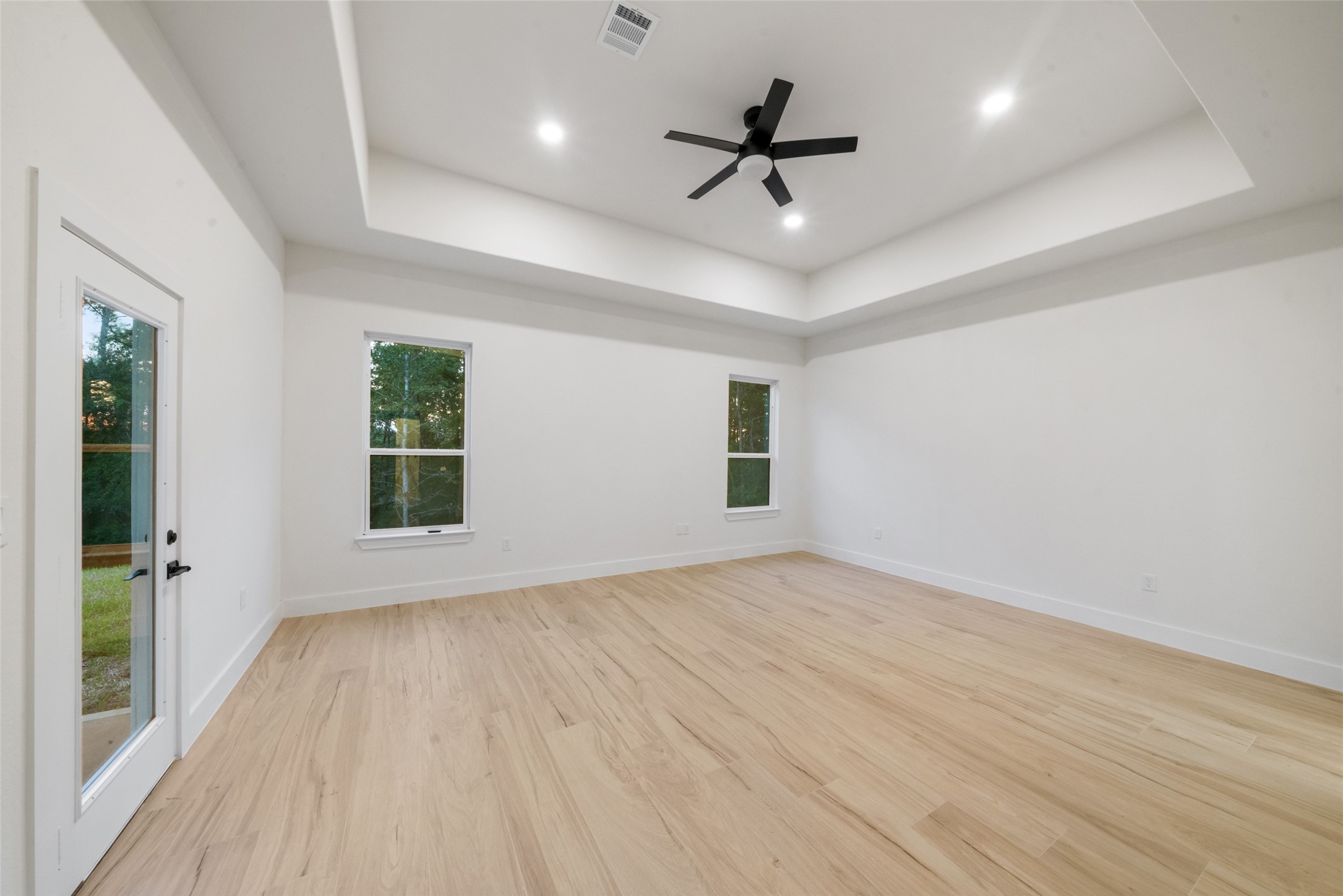 Another view of the spacious primary retreat highlighting its impressive tray ceiling, generous floor space, and beautiful contemporary finishes. Convenient access to the luxurious primary bathroom and private patio adds comfort and functionality.