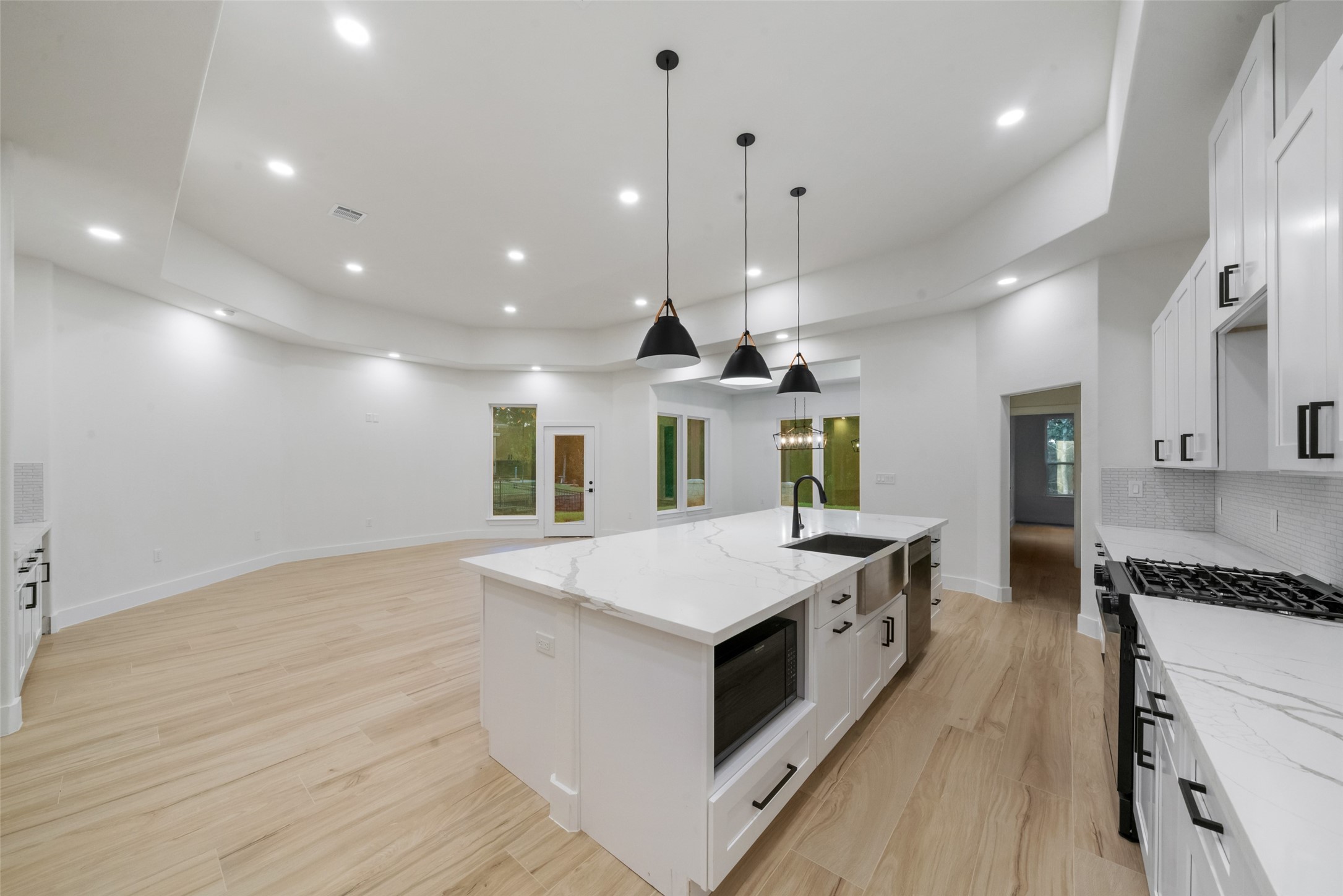 Gorgeous kitchen and living area featuring a grand center island with an undermount sink, marble-look countertops, and stylish black pendant lighting. The thoughtfully designed open floor plan offers effortless flow between cooking, dining, and entertaining spaces.