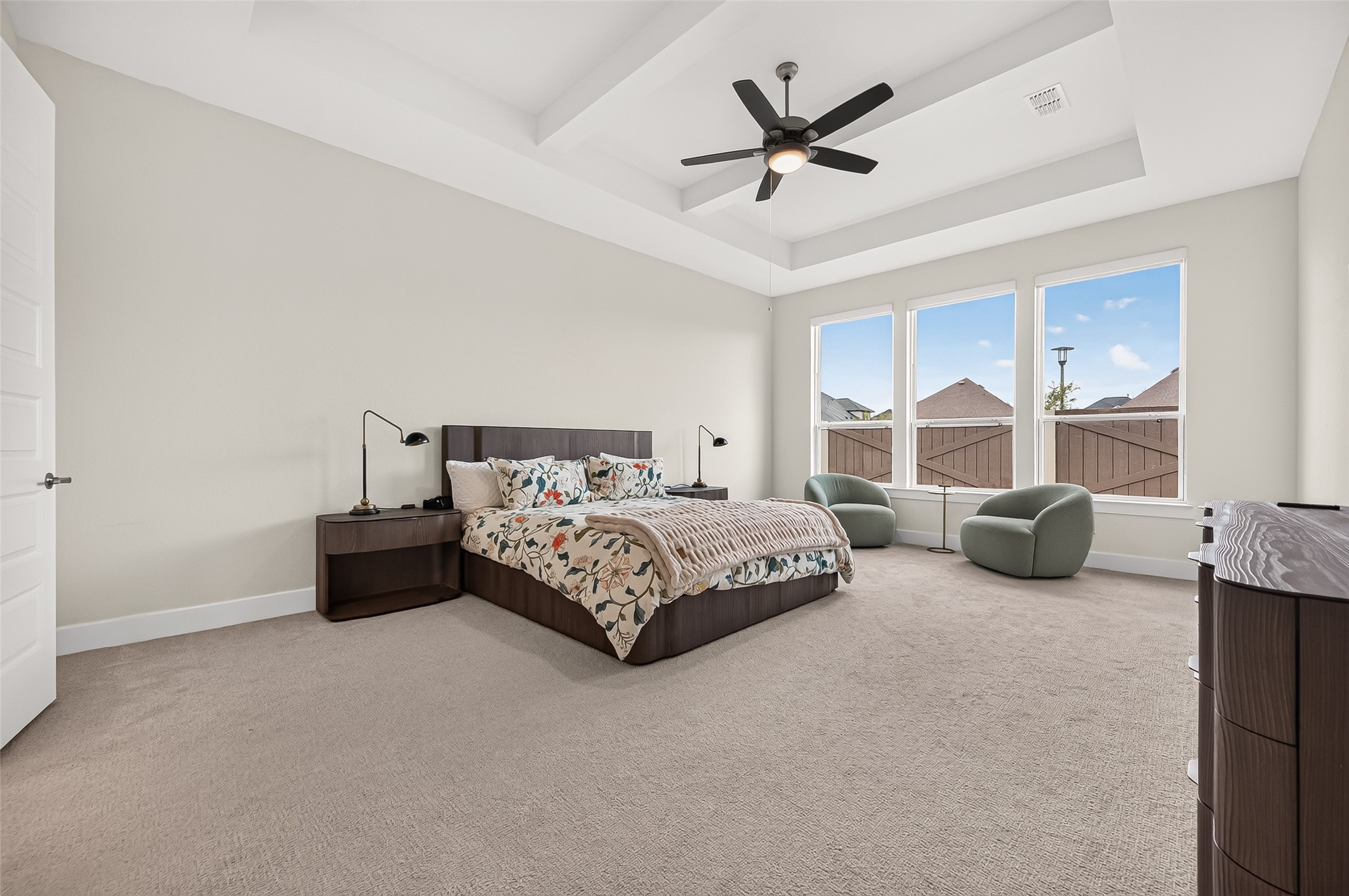 The luxurious primary suite is located downstairs and features high ceilings with a beautiful beam/coffered ceiling detail and a wall of windows.