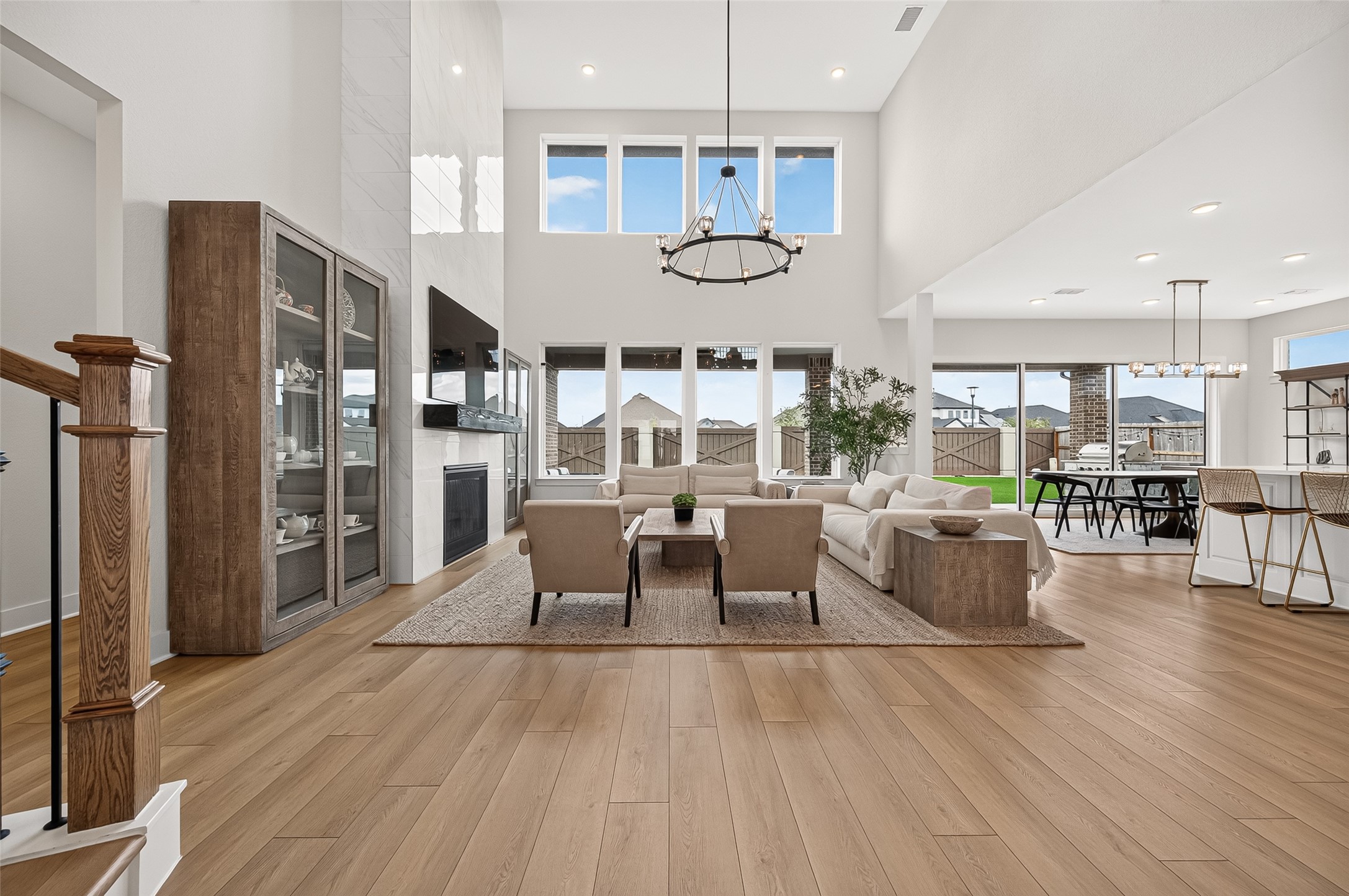 The open-concept family room showcases soaring ceilings, a wall of windows providing abundant natural light, and a dramatic floor-to-ceiling tiled fireplace.