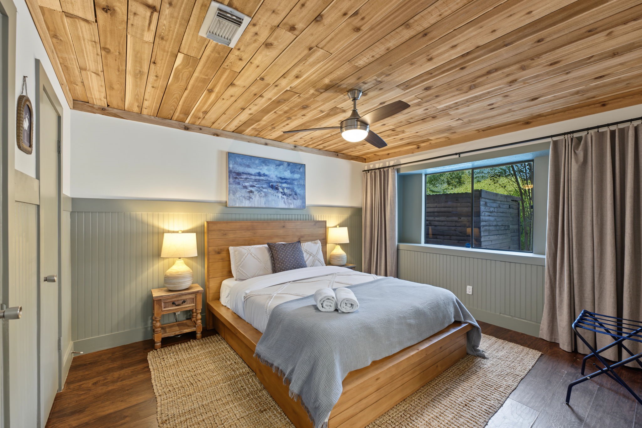 Downstairs primary retreat boasts a CEDAR PLANK CEILING, sage beadboard wainscoting and rich wood-look flooring!