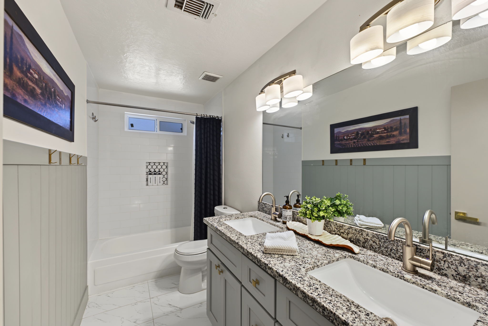 Secondary bath features a granite double vanity, subway tile tub/shower with decorative niche and marble-look tile floors!